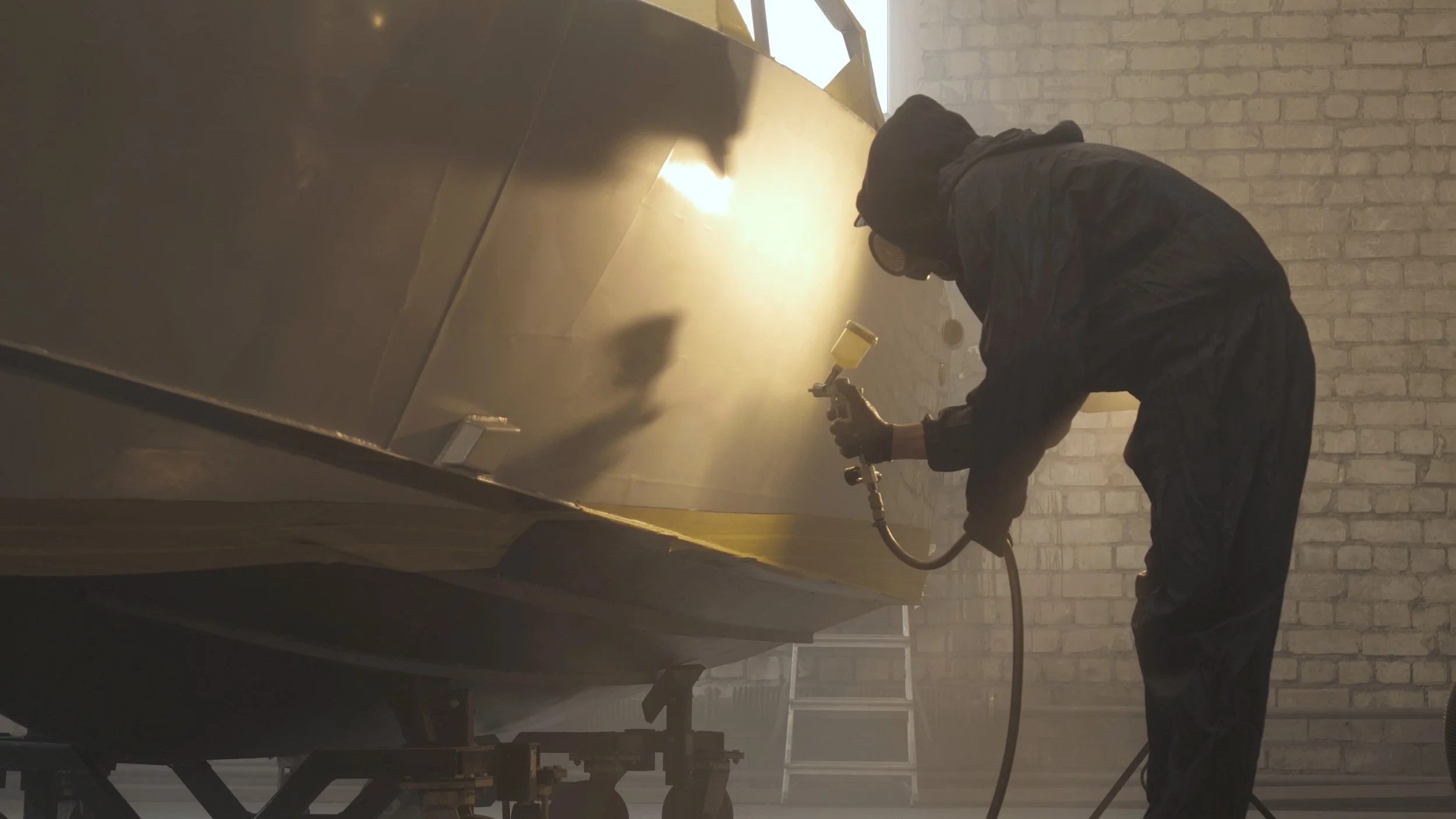 Person spray painting a large structure in an industrial setting.