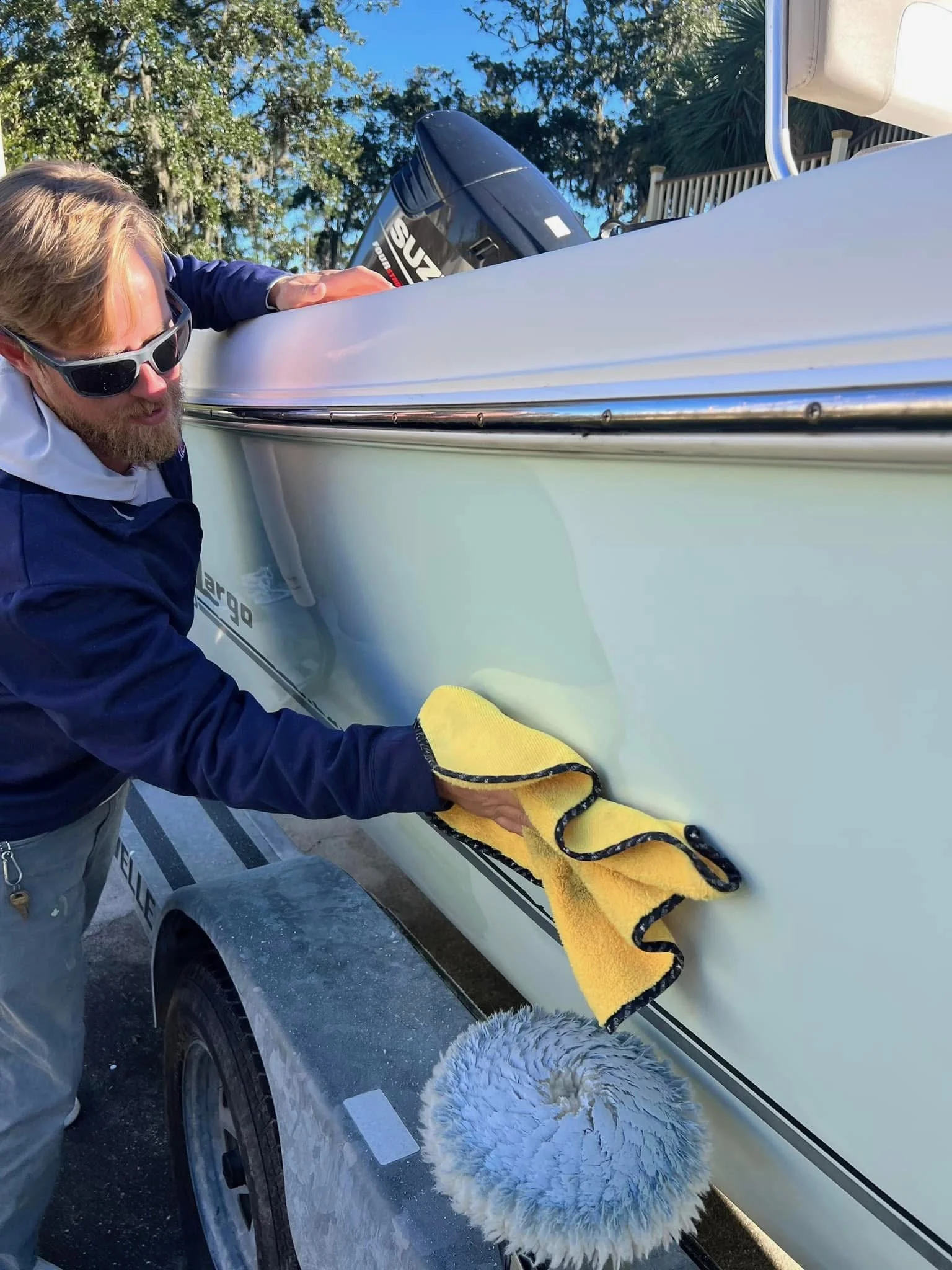Man cleaning a boat with a yellow cloth, with trailer and outboard motor visible