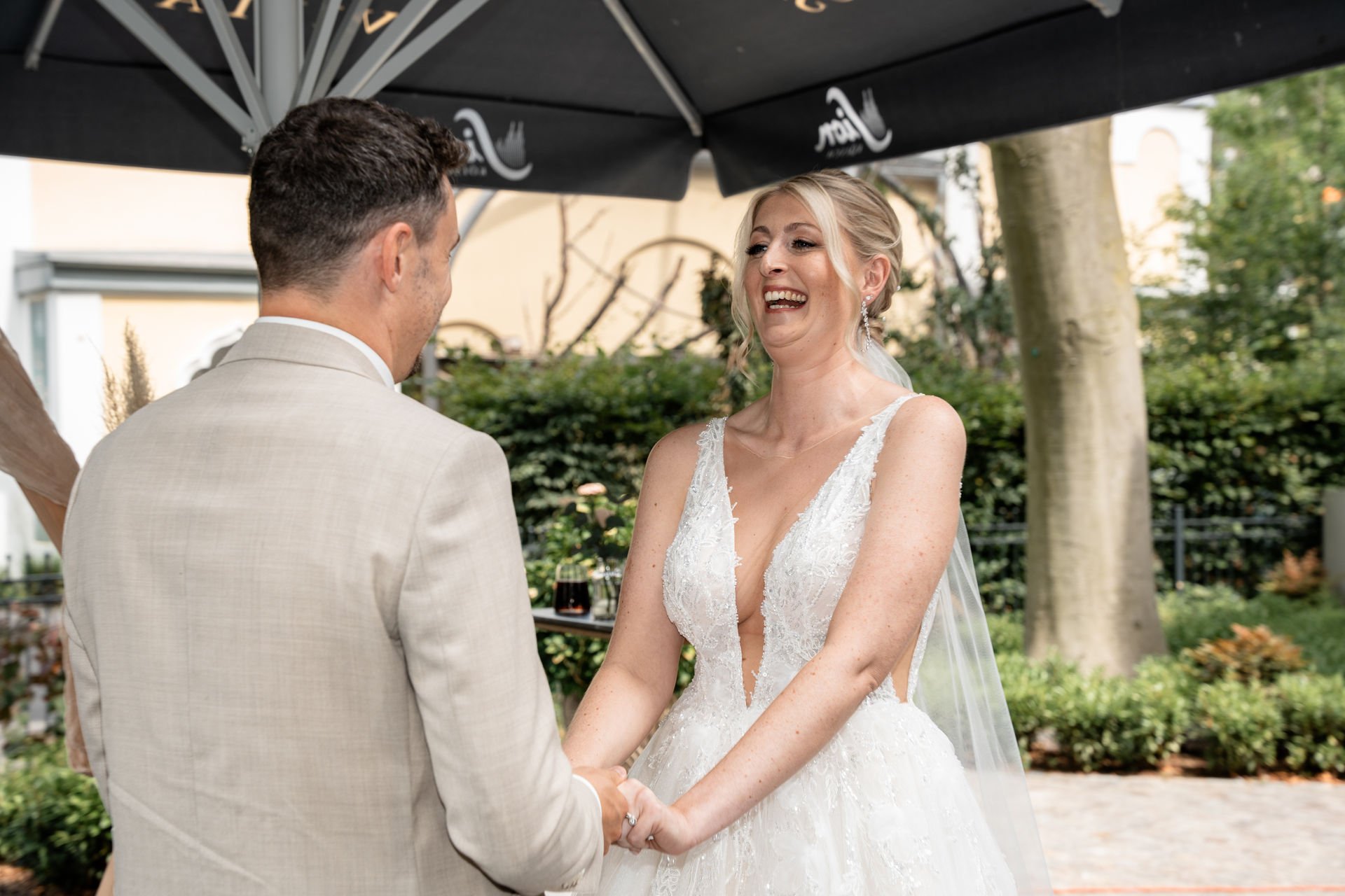Braut und Bräutigam halten Händchen bei ihrer Hochzeit im Freien, lächeln und betrachten sich.