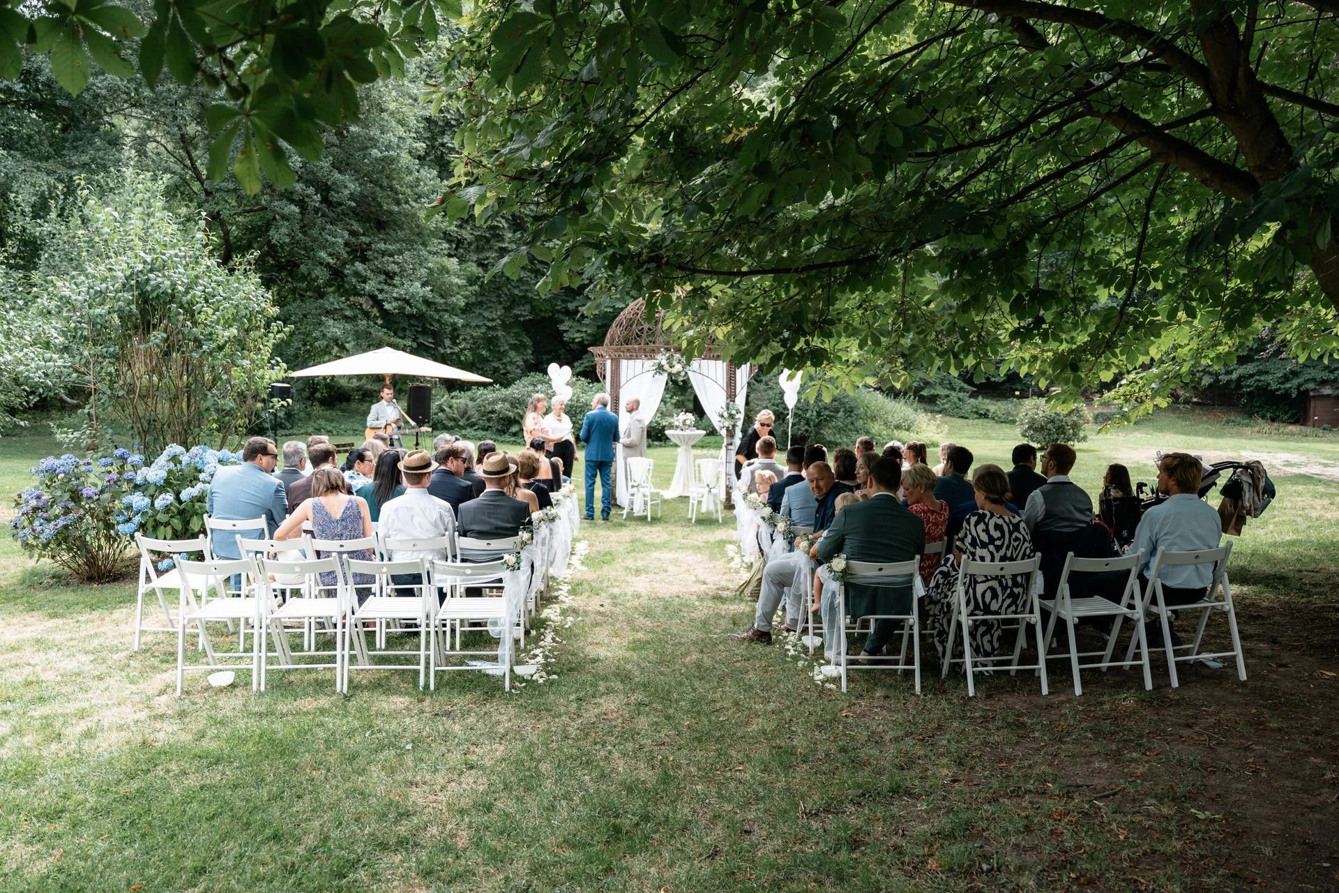Hochzeit im Garten mit Gästen, einem Hochzeitsbogen, Musik und Dekoration, Naturumgebung