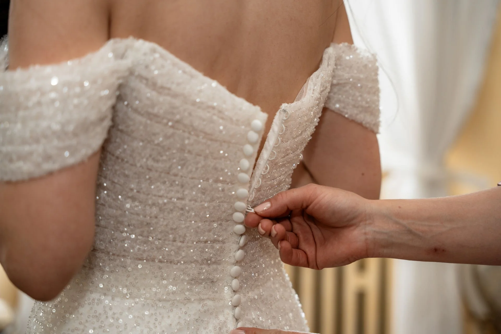 Ein Brautkleid mit Perlenknöpfen wird geschlossen.