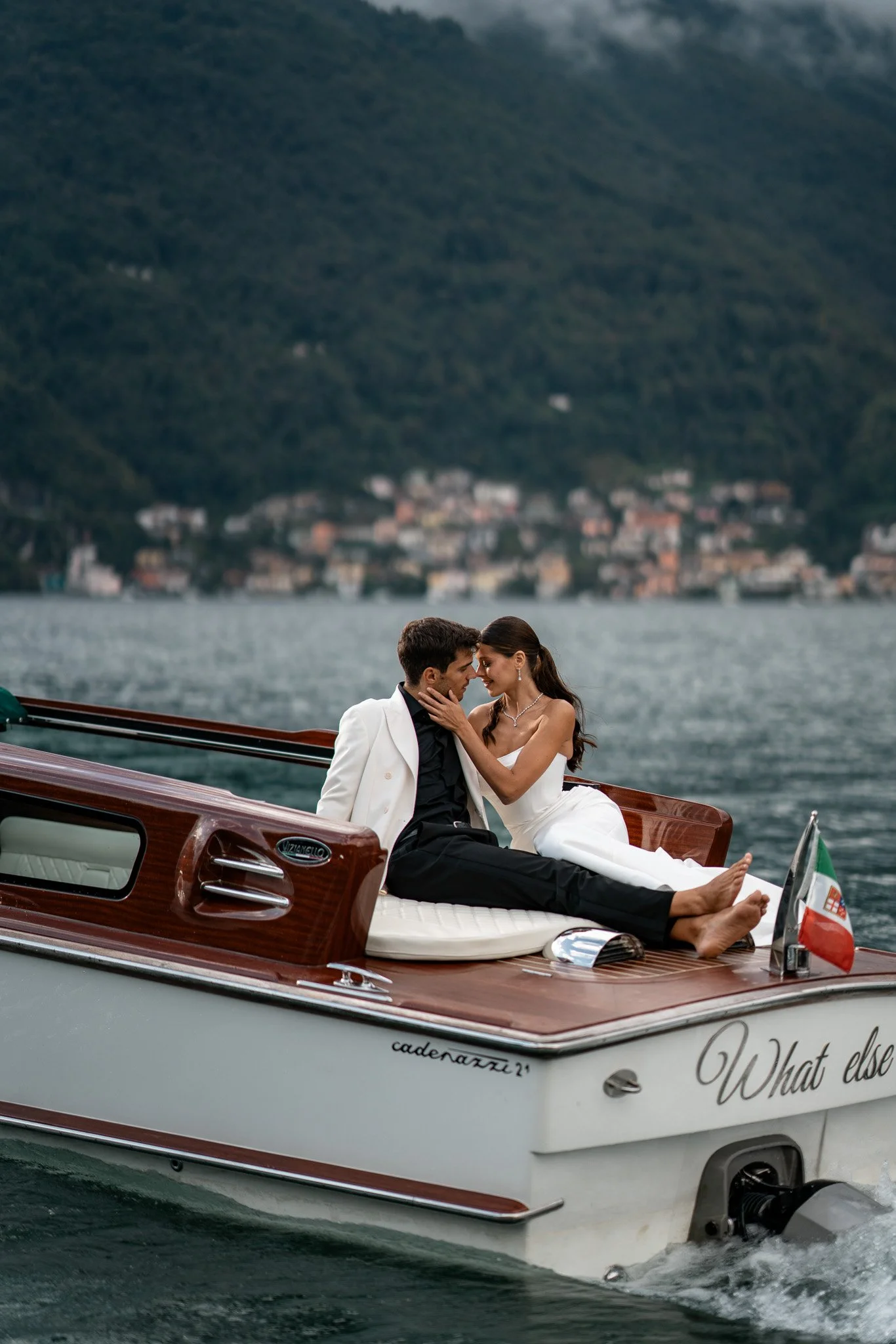 Ein Paar sitzt verliebt auf einem Motorboot im Wasser mit einem Hügel im Hintergrund.
