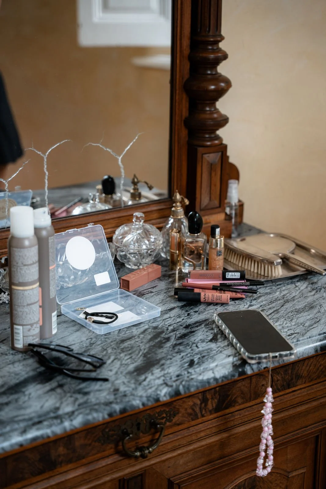 Schminktisch mit Make-up Produkten, Spiegel und Handyladegerät.