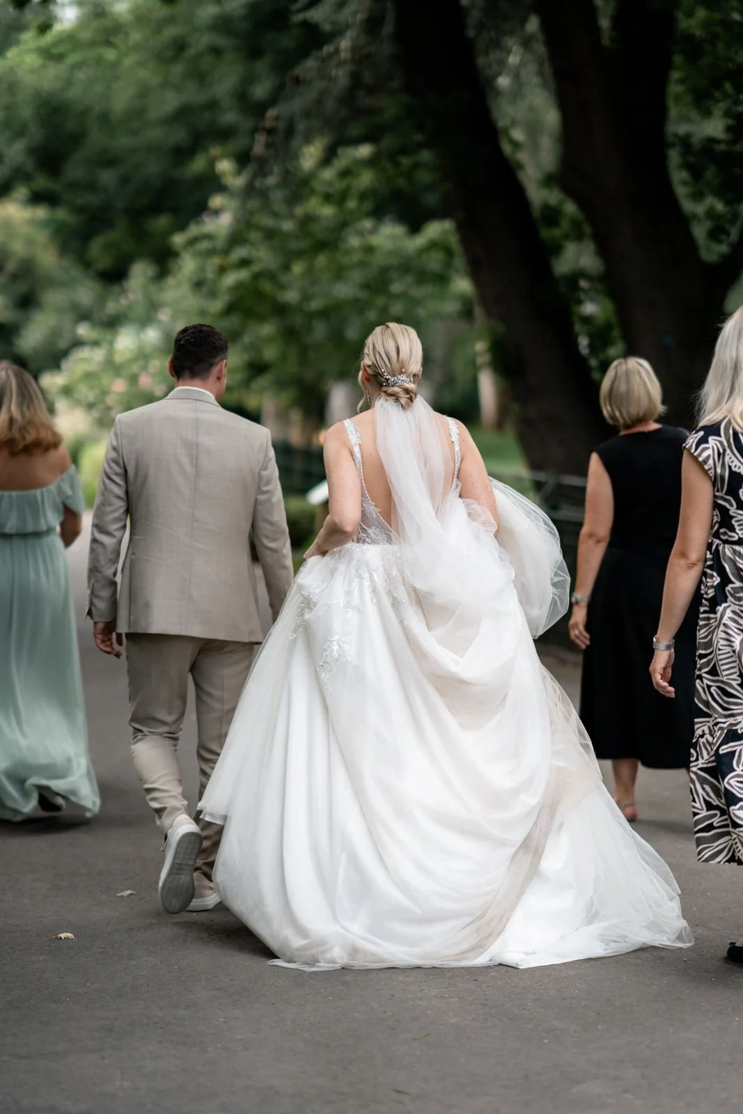 Braut in weißem Hochzeitskleid mit Begleitern, beim Spaziergang im Park.