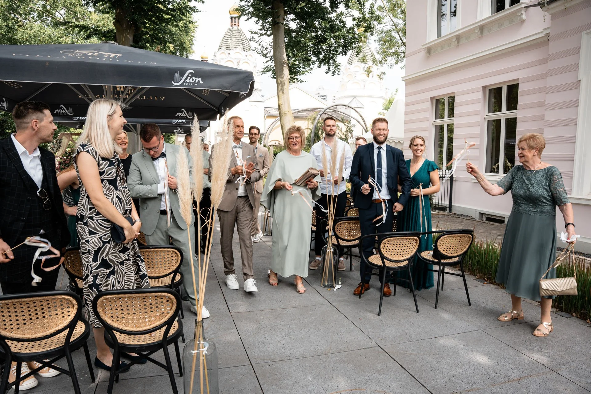 Menschen bei einer Feier im Freien, einige stehen, lächeln und halten Papierbänder, um eine Person auf der rechten Seite, die mit einer Papierrolle wedelt.