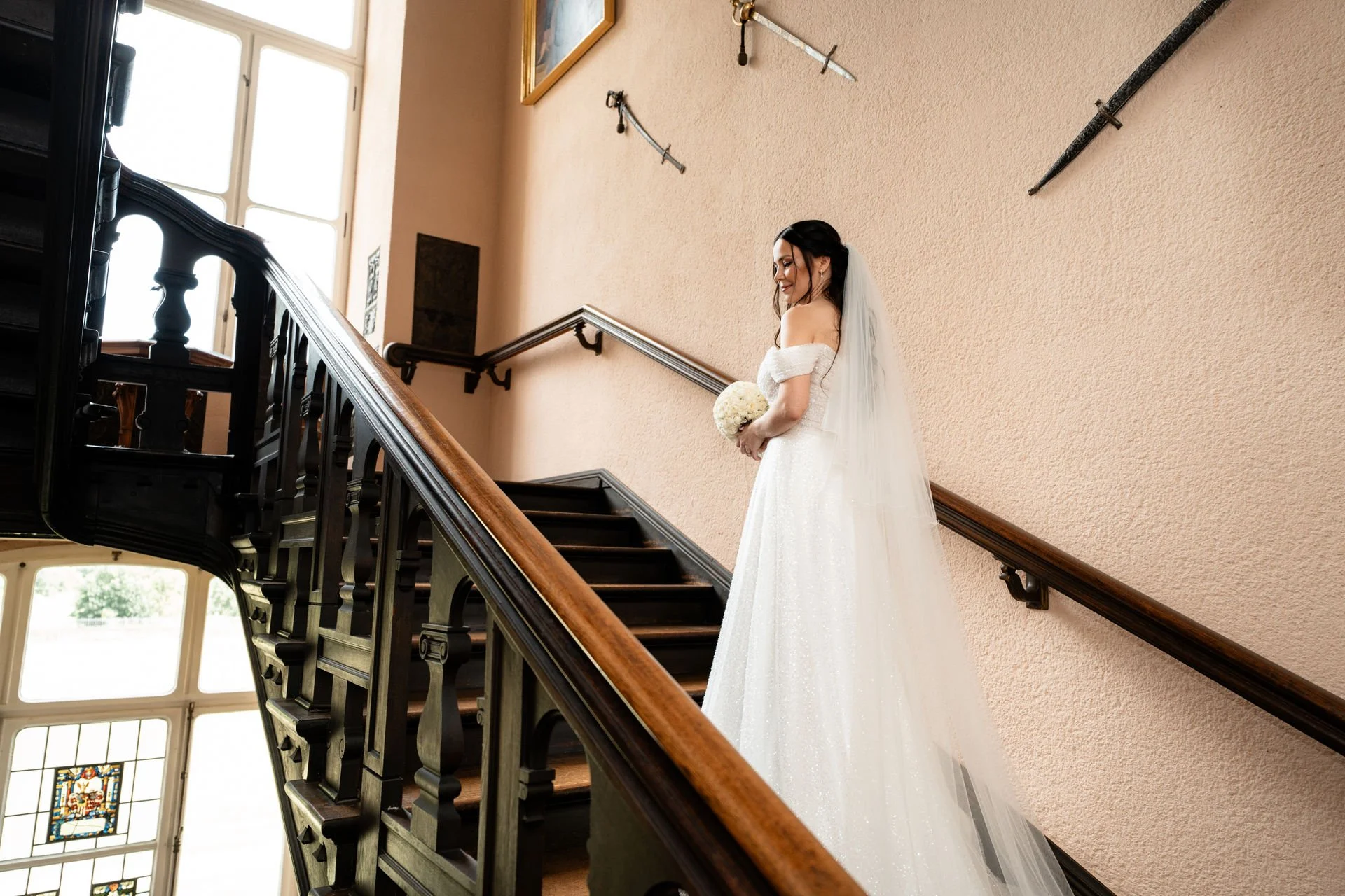 Braut in einem weißen Hochzeitskleid mit Schleier, die auf einer Treppe steht und einen Blumenstrauß hält.