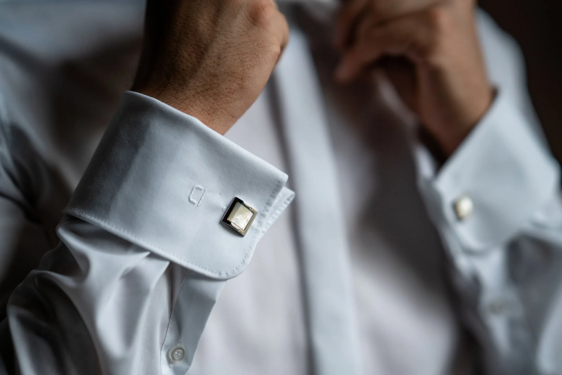 Nahaufnahme von Männern in weißen Hemden, die sich gegenseitig die Manschettenknöpfe anziehen.