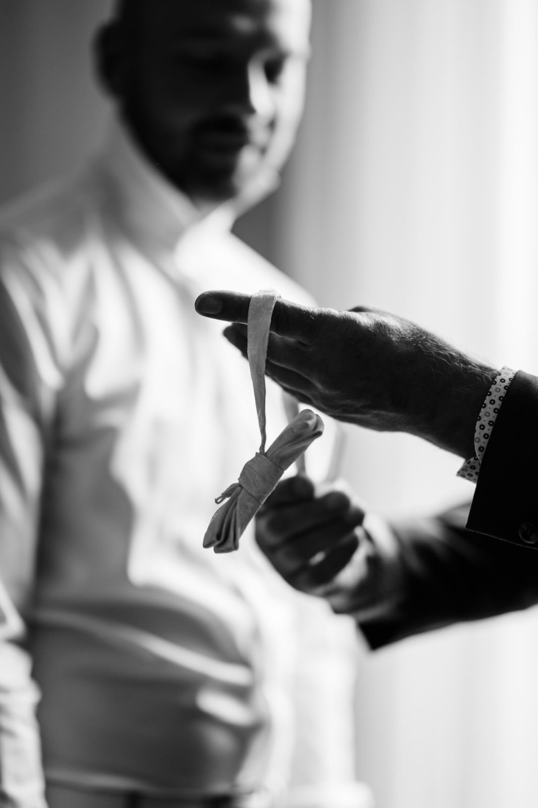 Nahaufnahme eines Mannes beim Tausch eines Armbandes gegen ein Geschenkbändchen, Schwarzweiß-Fotografie.