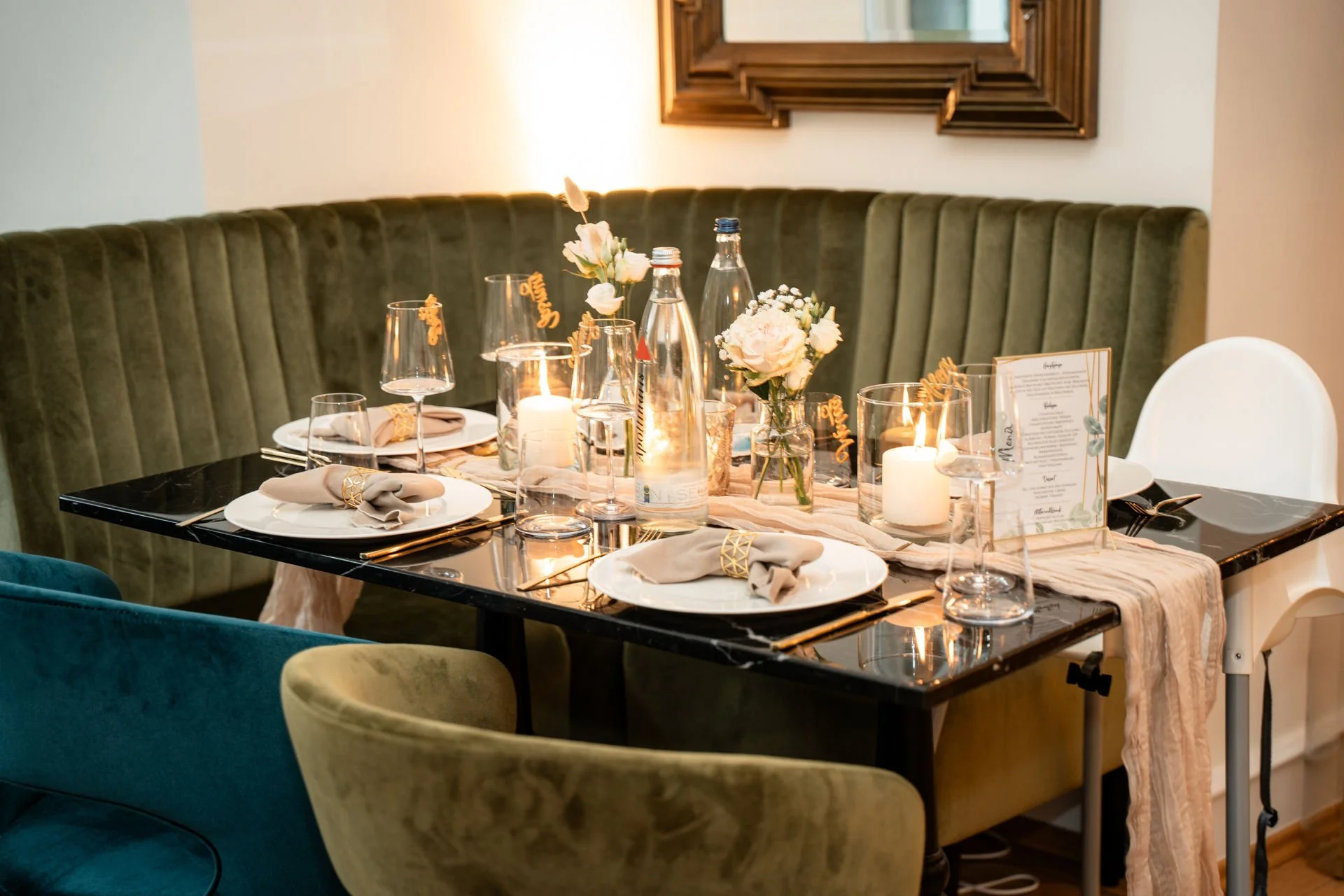 Elegant gedeckter Tisch mit Blumen, Kerzen, Wasserflaschen und Weingläsern in einem festlich dekorierten Raum.