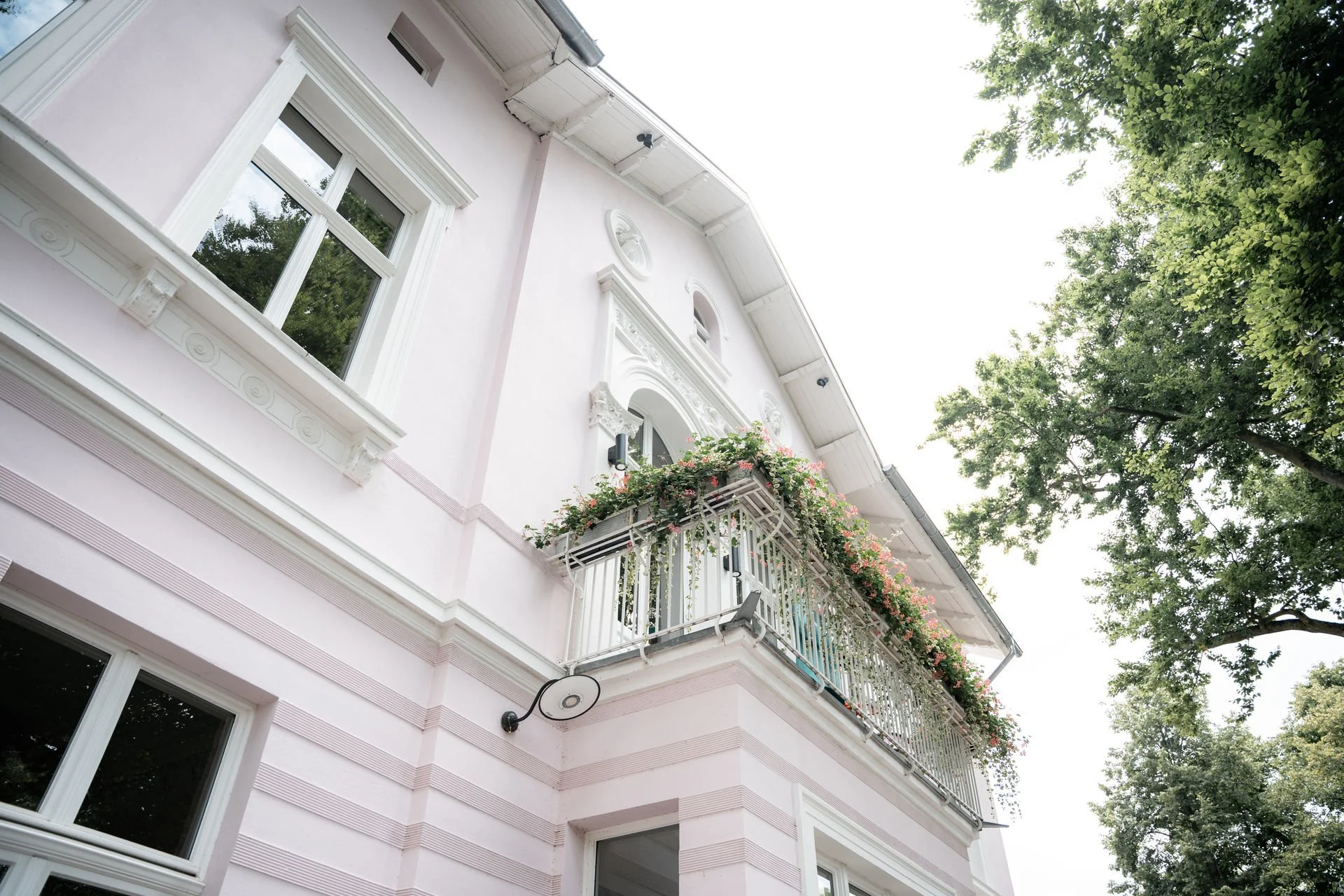 Fassade eines Hauses mit Balkon und Fenster, umgeben von Bäumen.