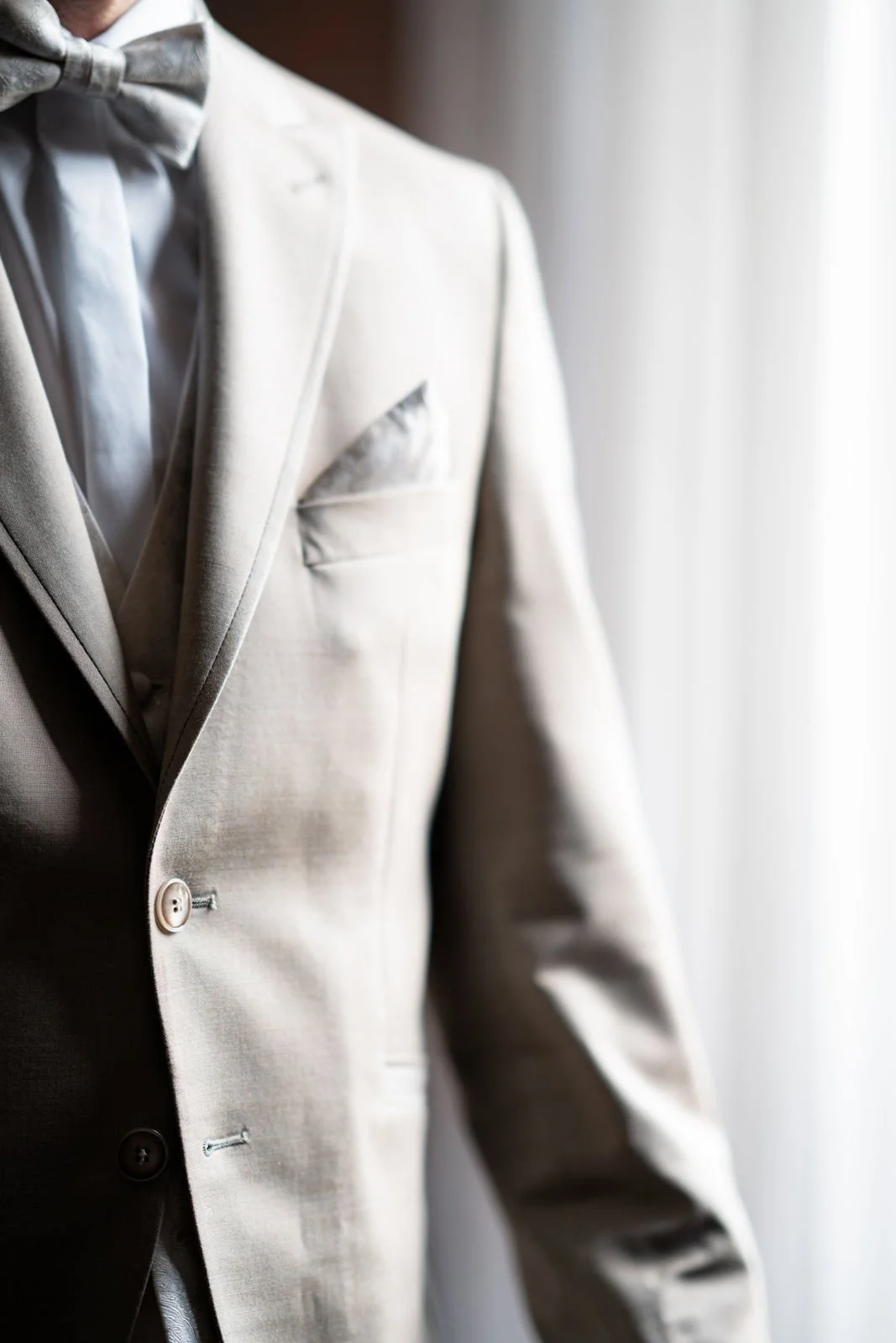 Nahaufnahme eines weißen Smoking-Jackets mit weißem Hemd und Fliege, vorbereitet für eine formelle Veranstaltung, vor einem hellen Vorhang.