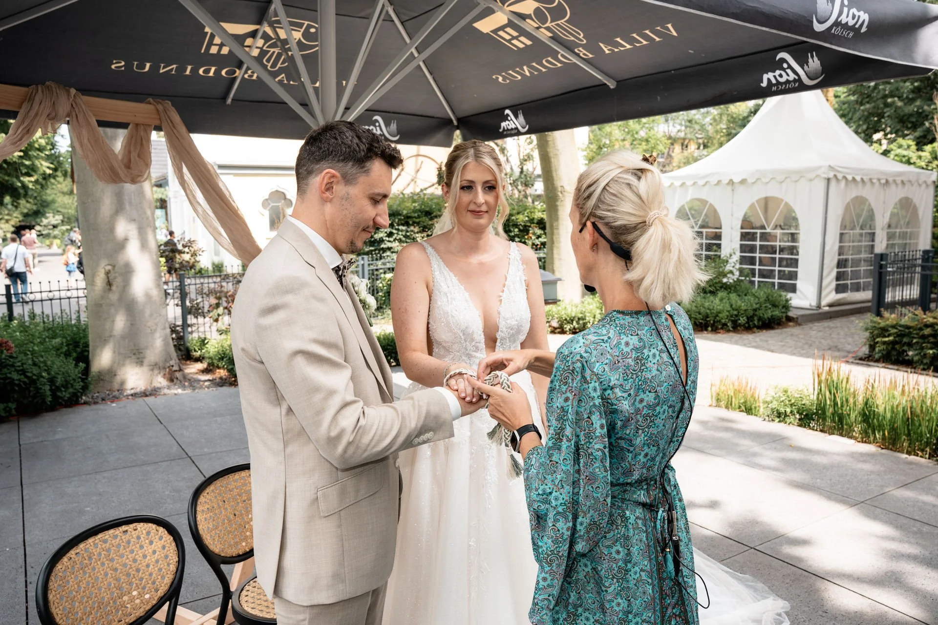 Trauung im Freien mit Brautpaar und Standesbeamtin unter einem großen Sonnenschirm in einem Garten