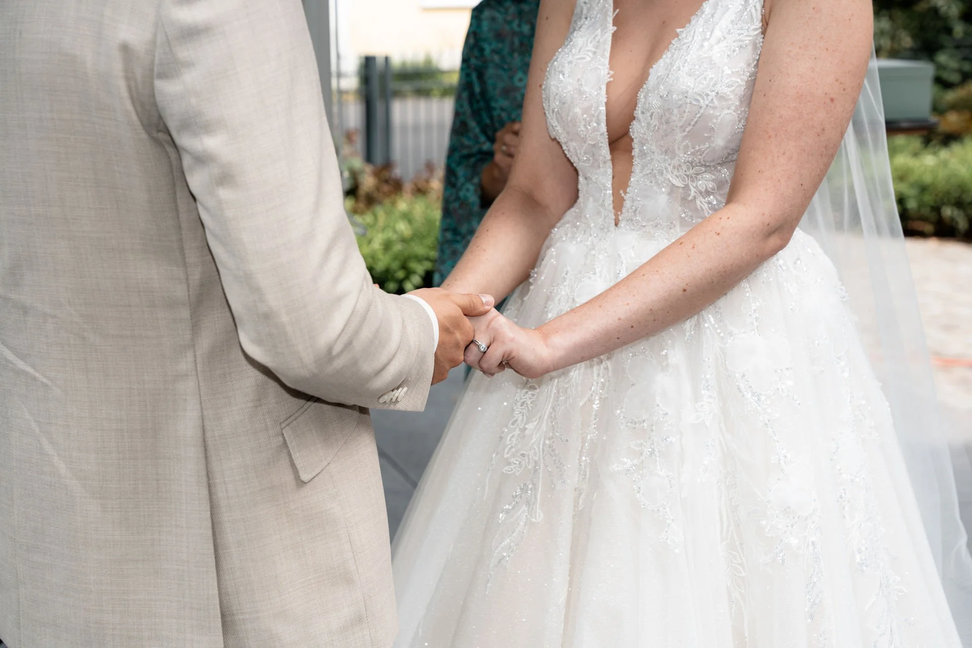 Braut und Bräutigam beim Händchenhalten bei ihrer Hochzeit, Nahaufnahme der Hände und des Brautkleides.