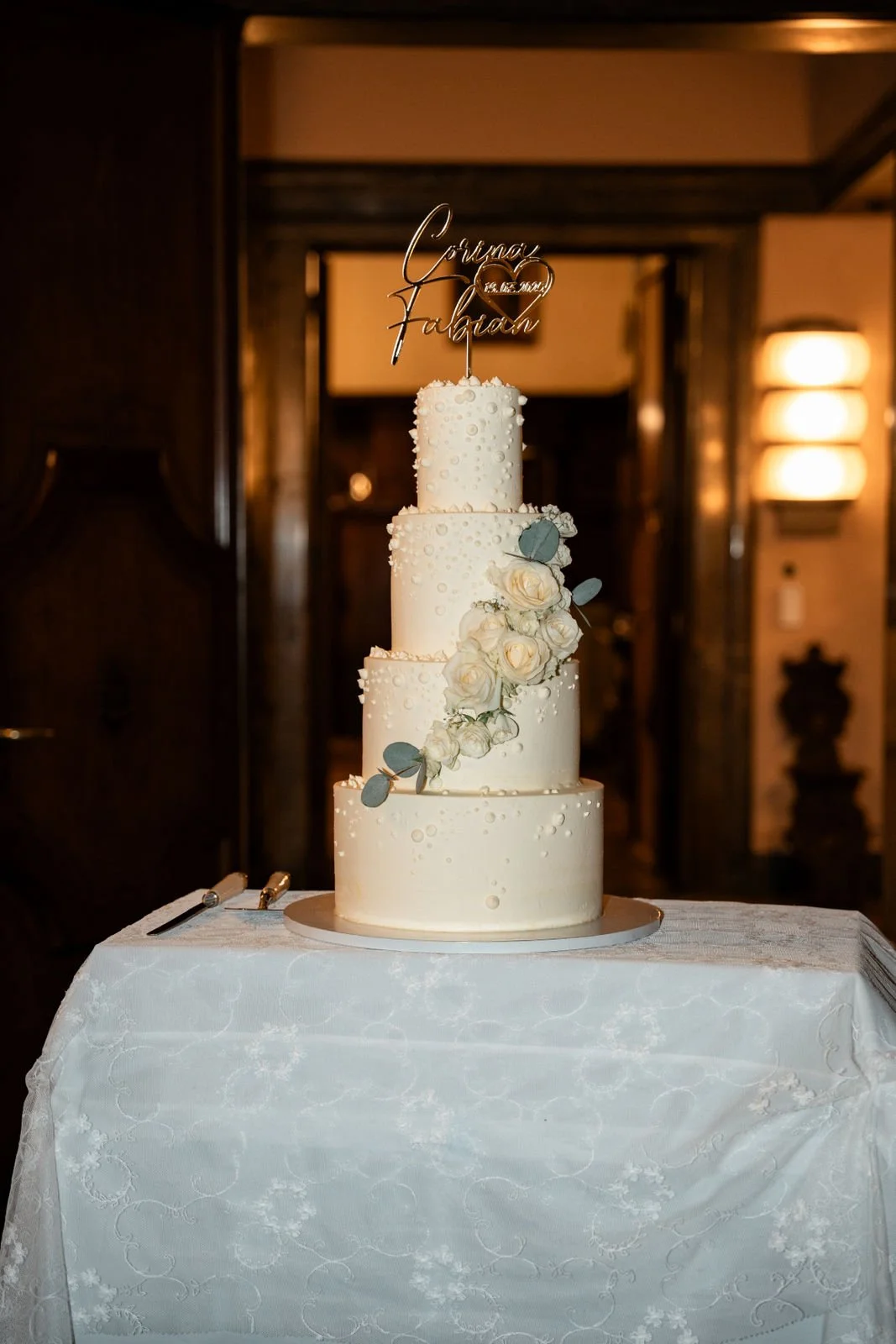 Vierstöckige weiße Hochzeitstorte mit Blumen und personalisiertem Cake Topper.