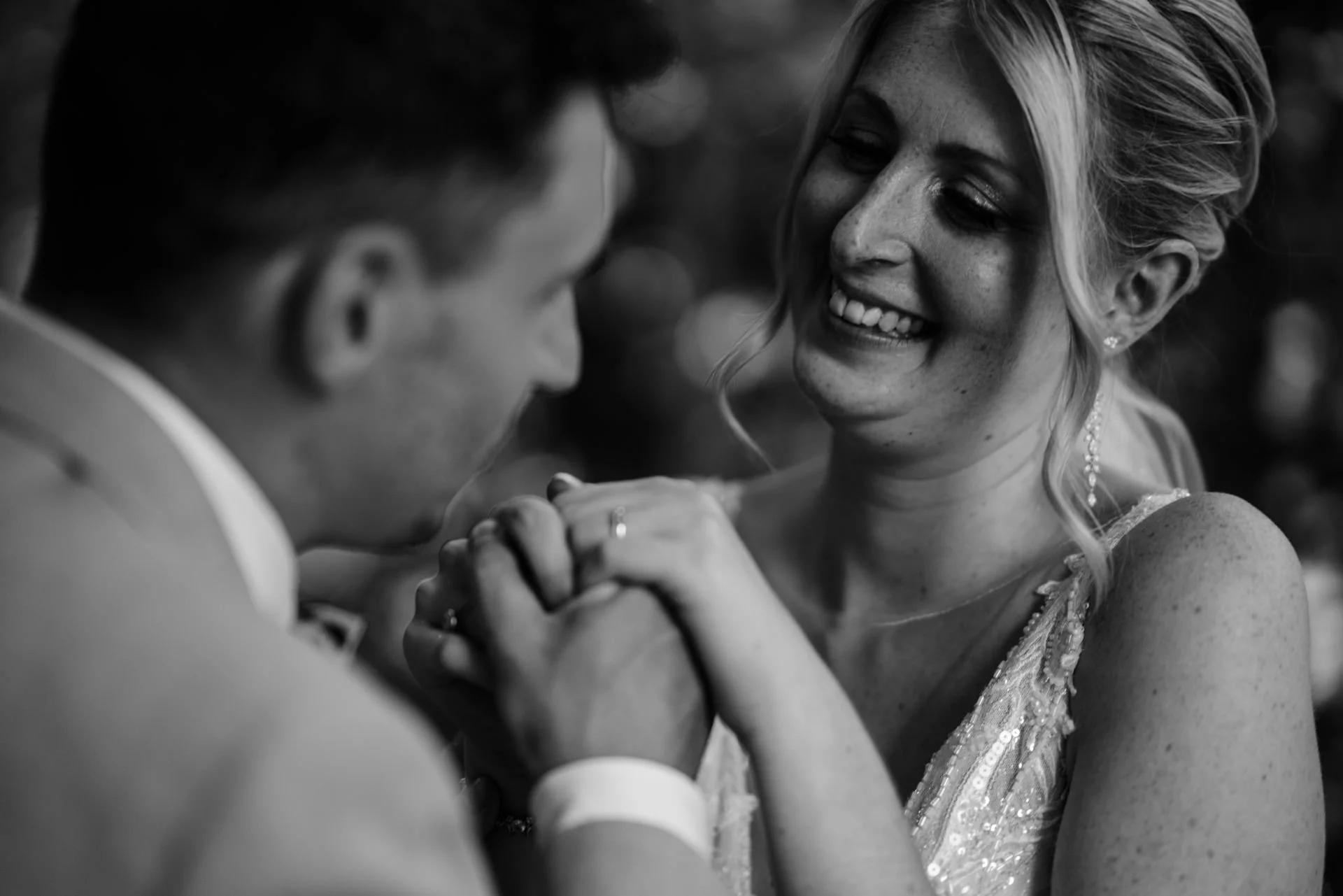 Ein lachendes Paar bei einer Hochzeit, das Händchen hält, in Schwarz-Weiß aufgenommen.