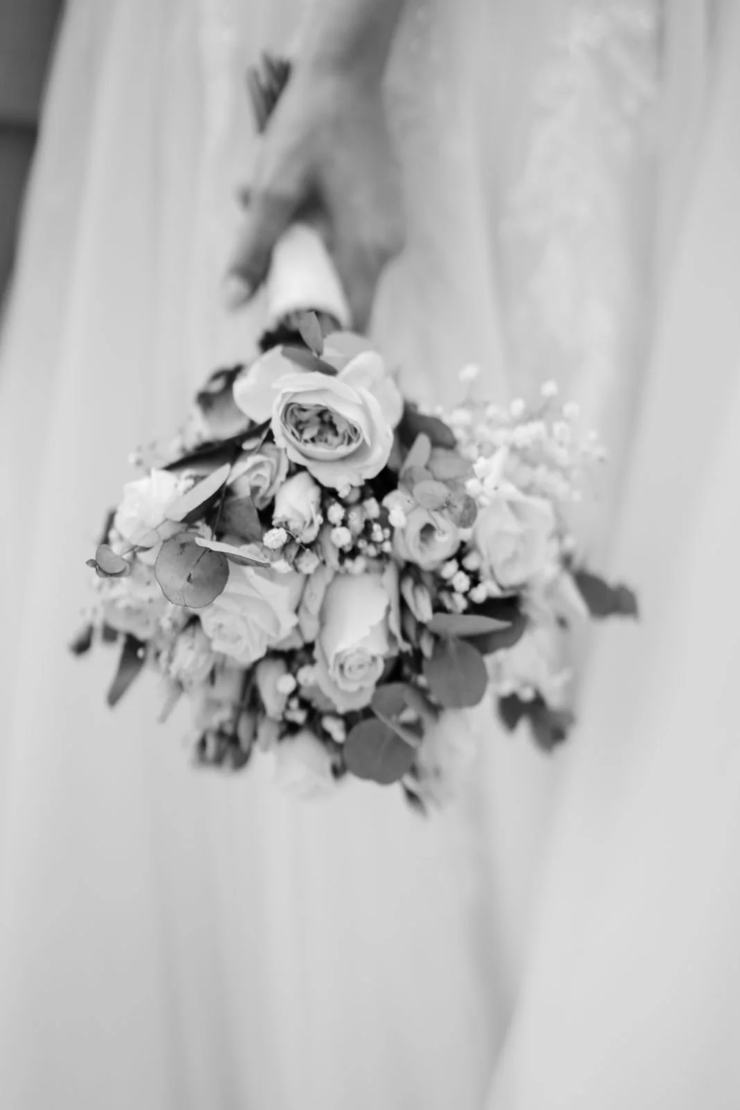 Schwarz-weiß-Foto einer Brautjungfer, die einen Brautstrauß aus Rosen und anderen Blumen hält.