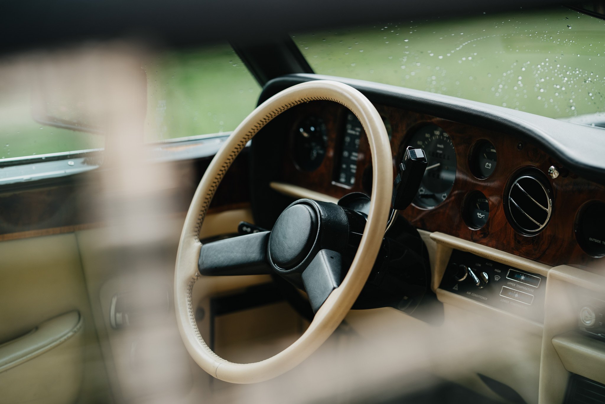 Der Blick auf das Armaturenbrett und das Lenkrad eines klassischen Autos mit Holzdekor, das bei Regen im Inneren nass ist.