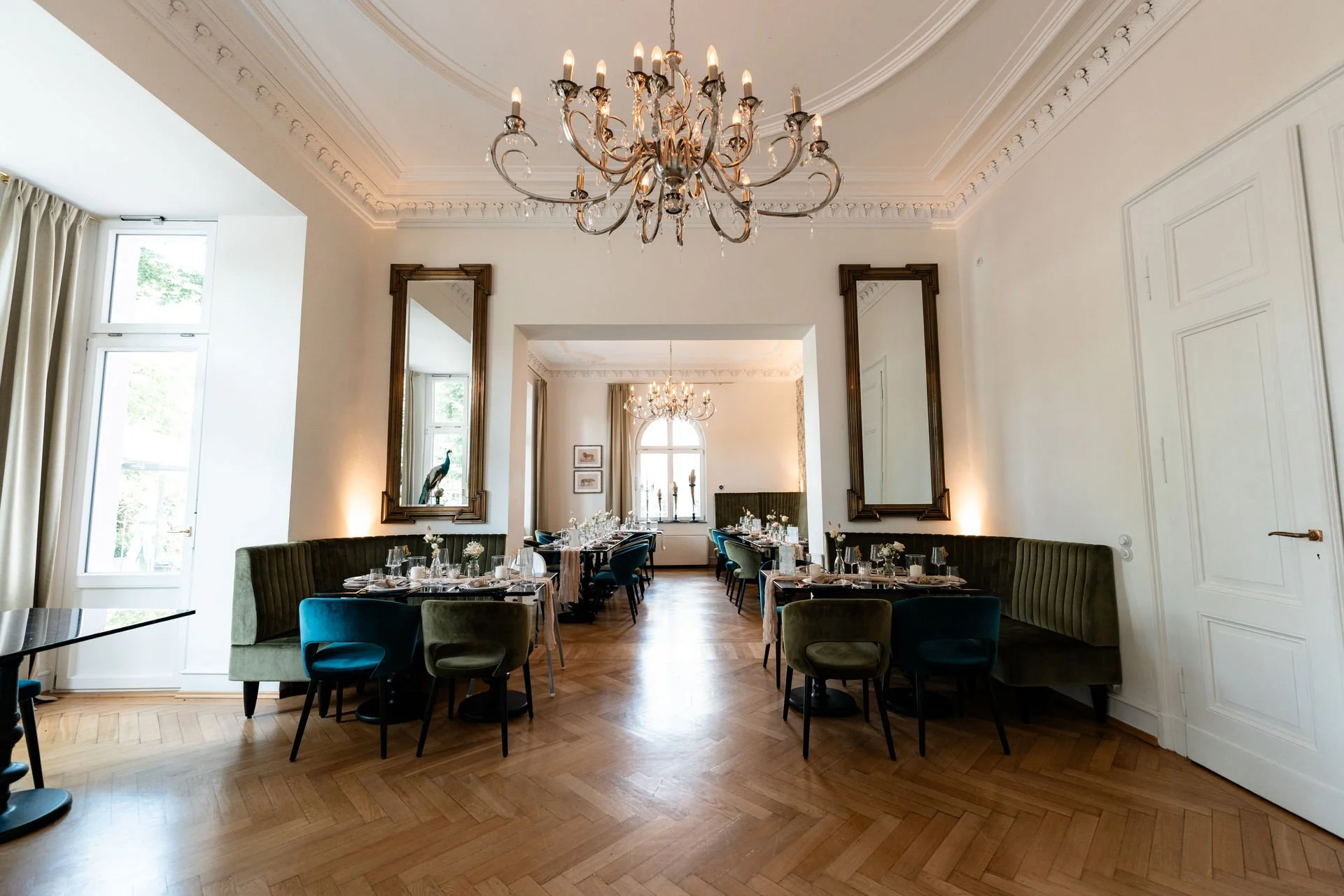 Eleganter Speisesaal mit gehobener Inneneinrichtung, Kronleuchtern, gedeckten Tischen, hohen Fenstern und Spiegelwänden.