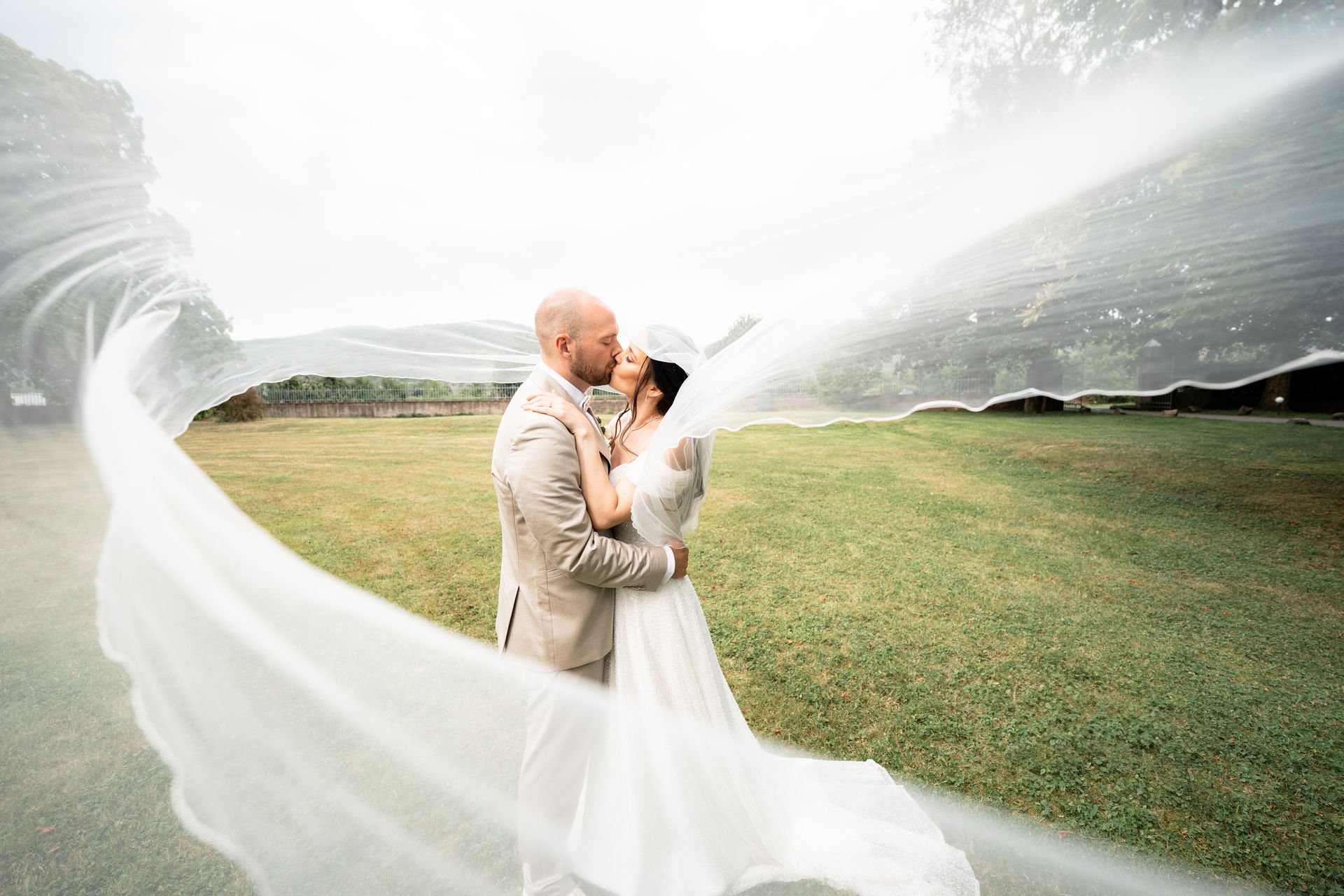 Braut und Bräutigam küssen sich im Freien, eingehüllt in die Schleppe des Brautkleides, die den Rahmen bildet.