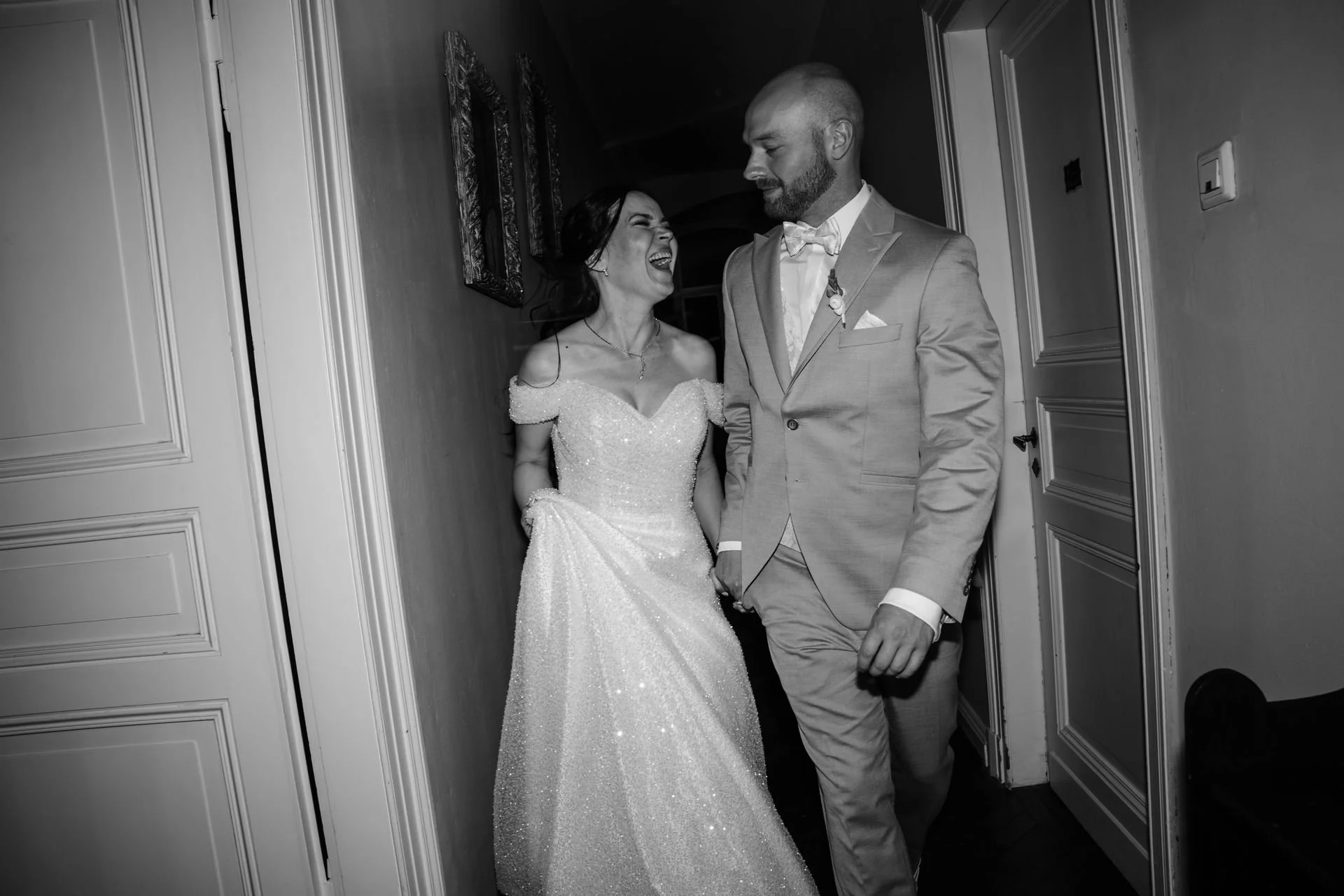 Braut und Bräutigam lachen zusammen in einem Flur während ihrer Hochzeitsfeier, schwarz-weiß Foto.
