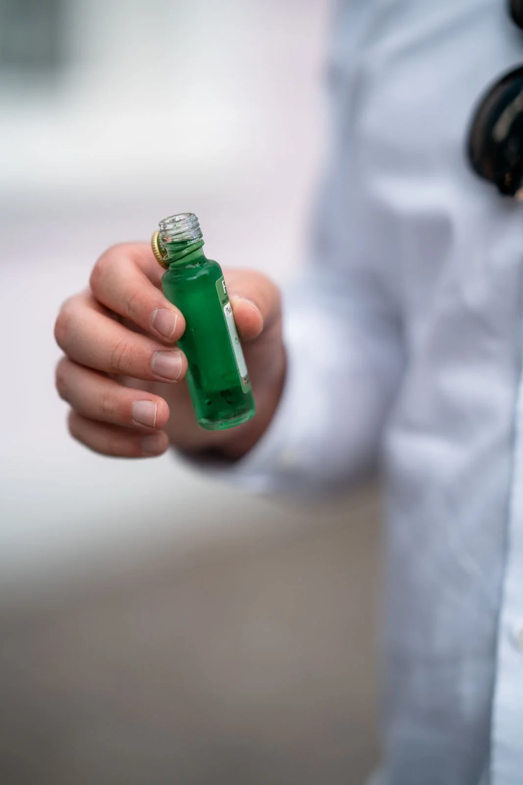 Ein Arzt hält eine kleine grüne Flasche mit Flüssigkeit in der Hand, wobei der Fokus auf der Flasche liegt.