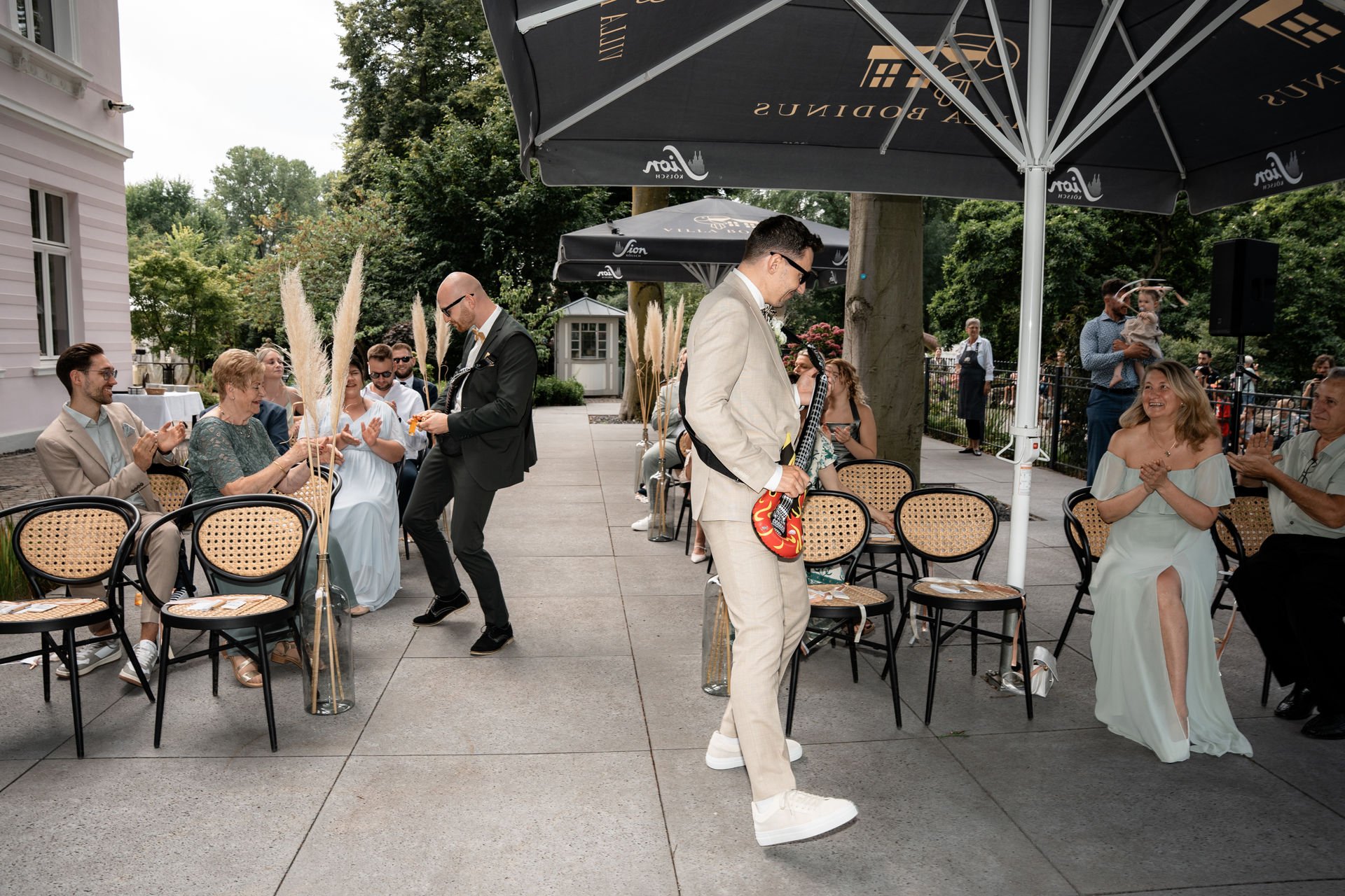Sängertreffen im Freien, mit Gästen, die applaudieren, und Musikern, die auf einer kleinen Bühne spielen.