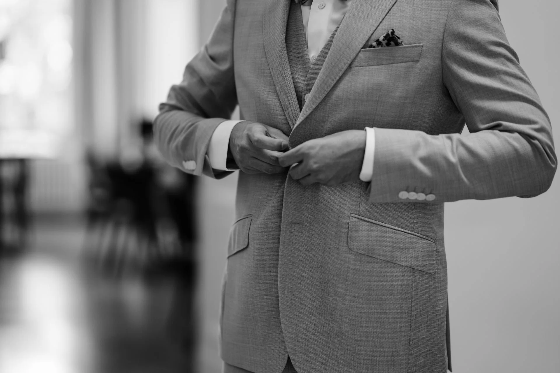 Ein Mann in einem Anzug richtet den Knopf seines Anzugs. Das Bild ist in Schwarz-Weiß.
