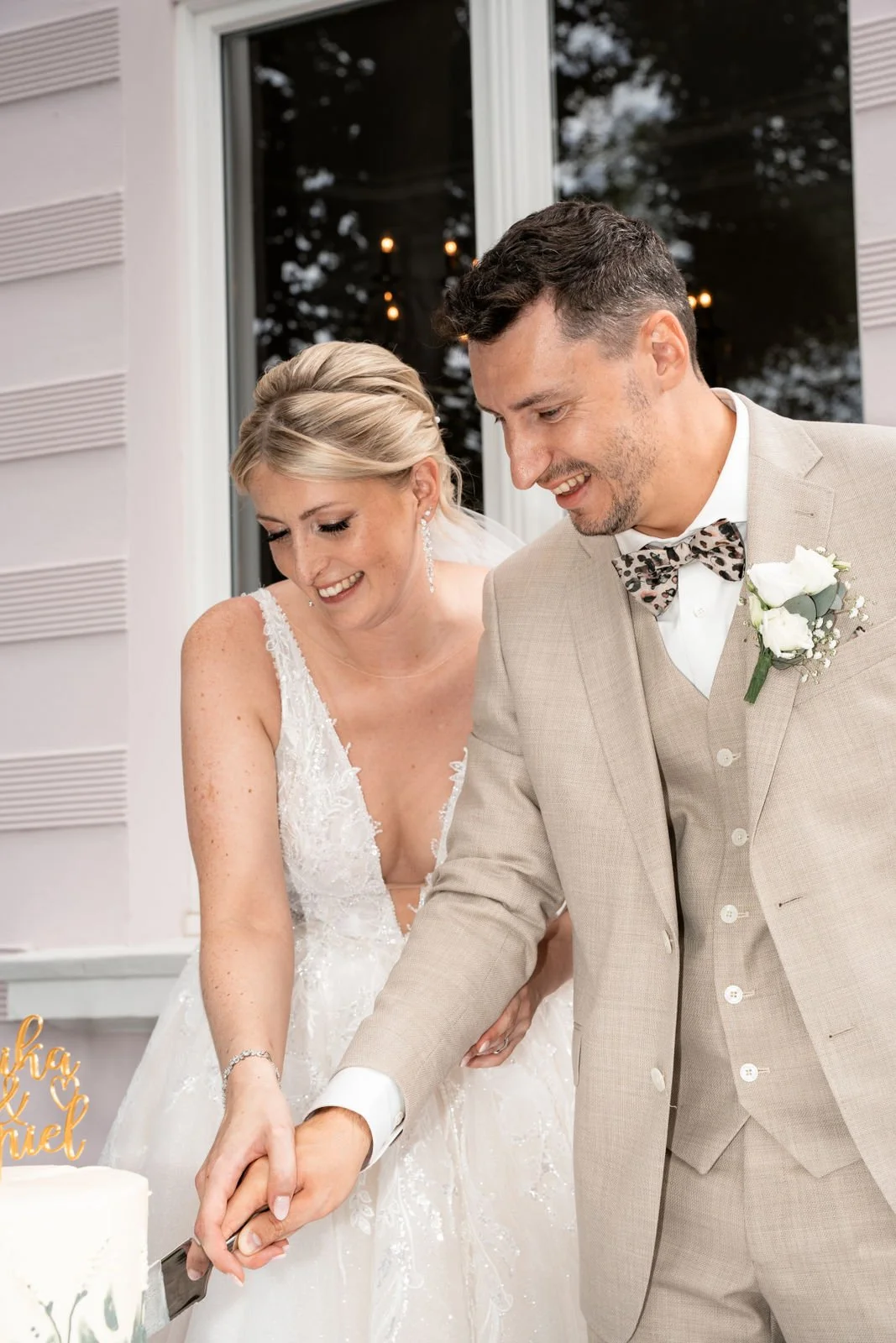 Braut und Bräutigam beim gemeinsamen Anschneiden der Hochzeitstorte, beide lächeln glücklich.