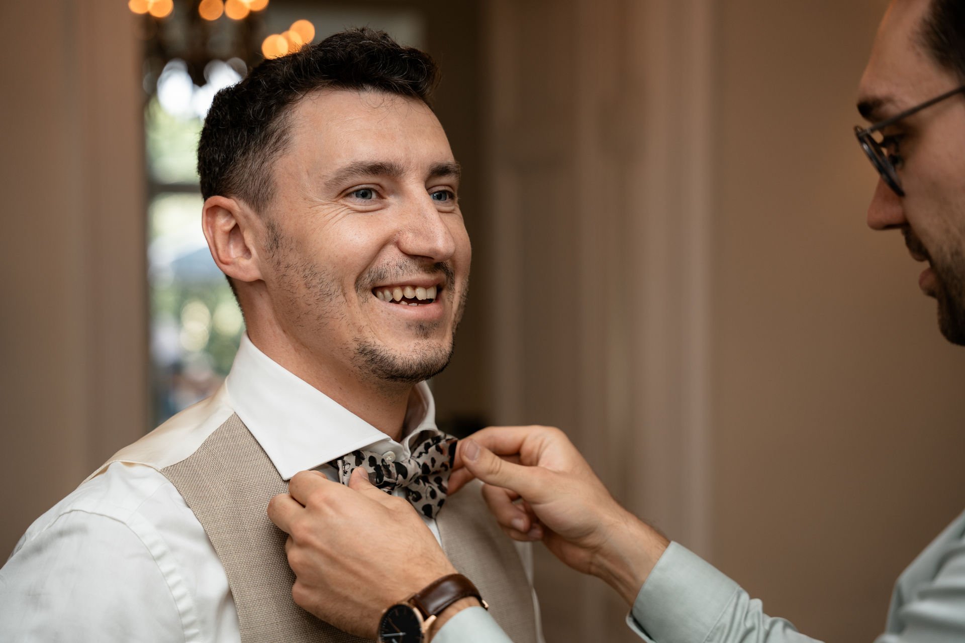 Ein Mann wird von einem anderen Mann bei einer Hochzeit oder formellen Veranstaltung den Krawattenknoten angepasst.