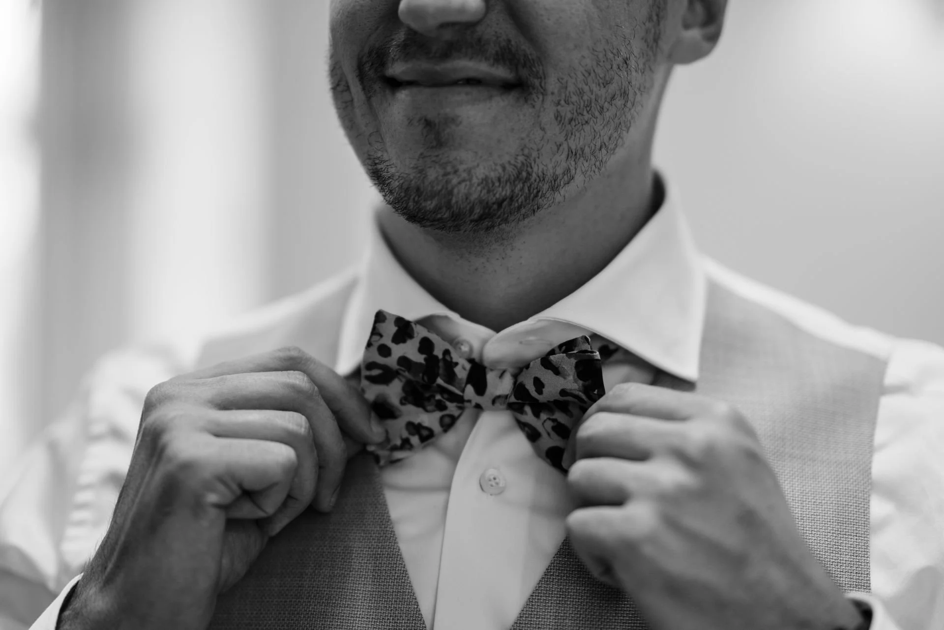 Ein Mann richtet eine Schleife an seiner Fliege, trägt ein weißes Hemd und eine Weste, Nahaufnahme des Gesichts und Oberkörpers, Schwarz-Weiß-Foto.