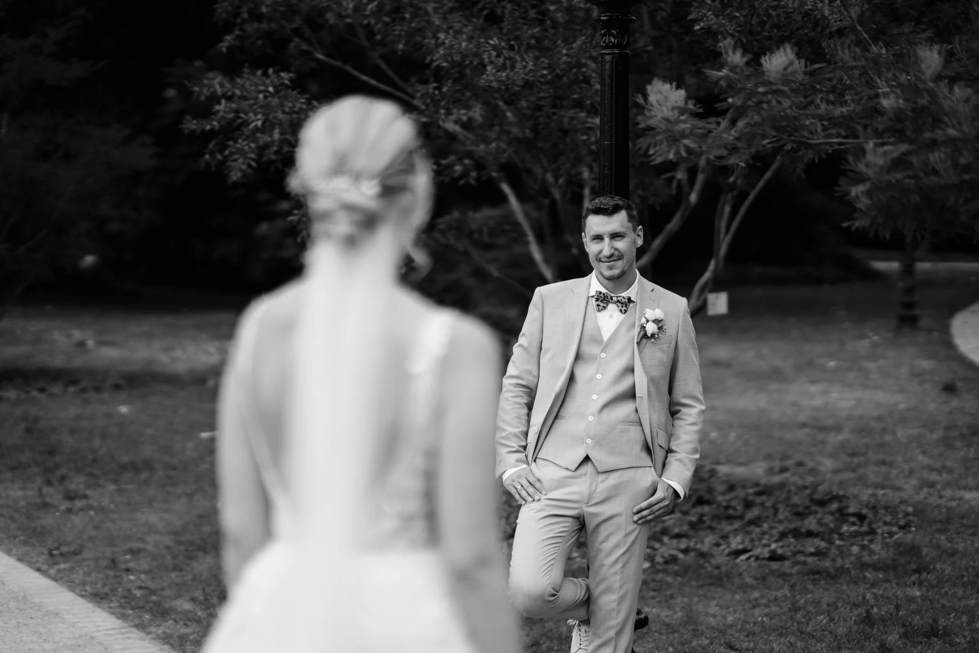 Ein Mann in einem Anzug, der in einem Park steht und auf eine Frau wartet, die im Vordergrund unscharf ist.