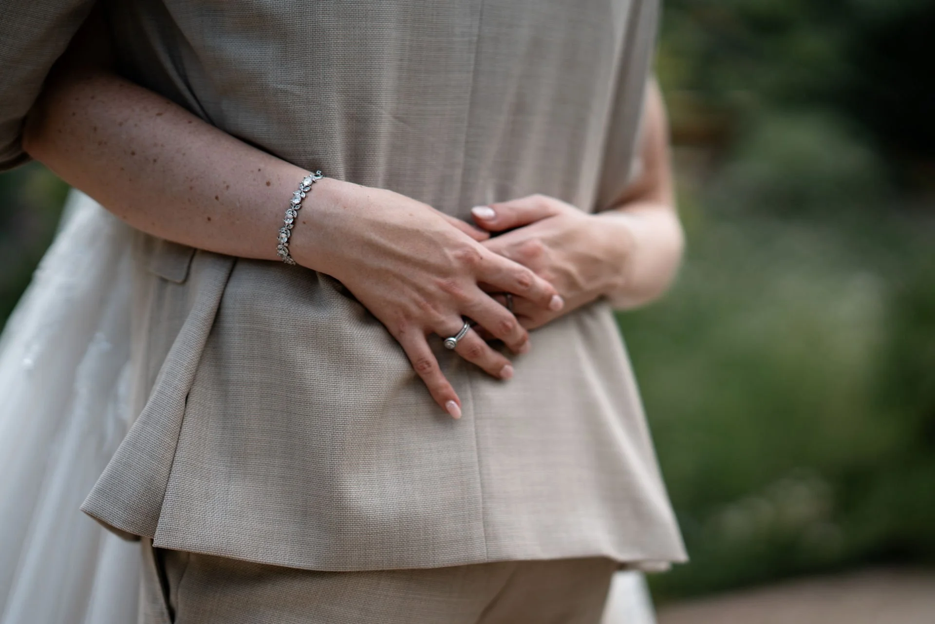Nahaufnahme von Händen, die eine Ehefrau halten, mit Eheringen und einer Armbanduhr, bei einer Hochzeit im Freien.