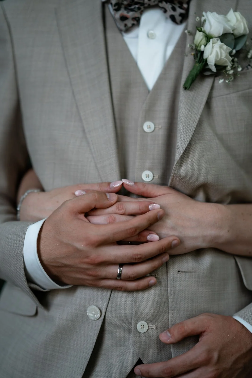 Nahaufnahme eines Paares, das sich bei einer Hochzeit umarmt, mit Fokus auf ihre Handhaltung und das Brautpaar-Outfit.