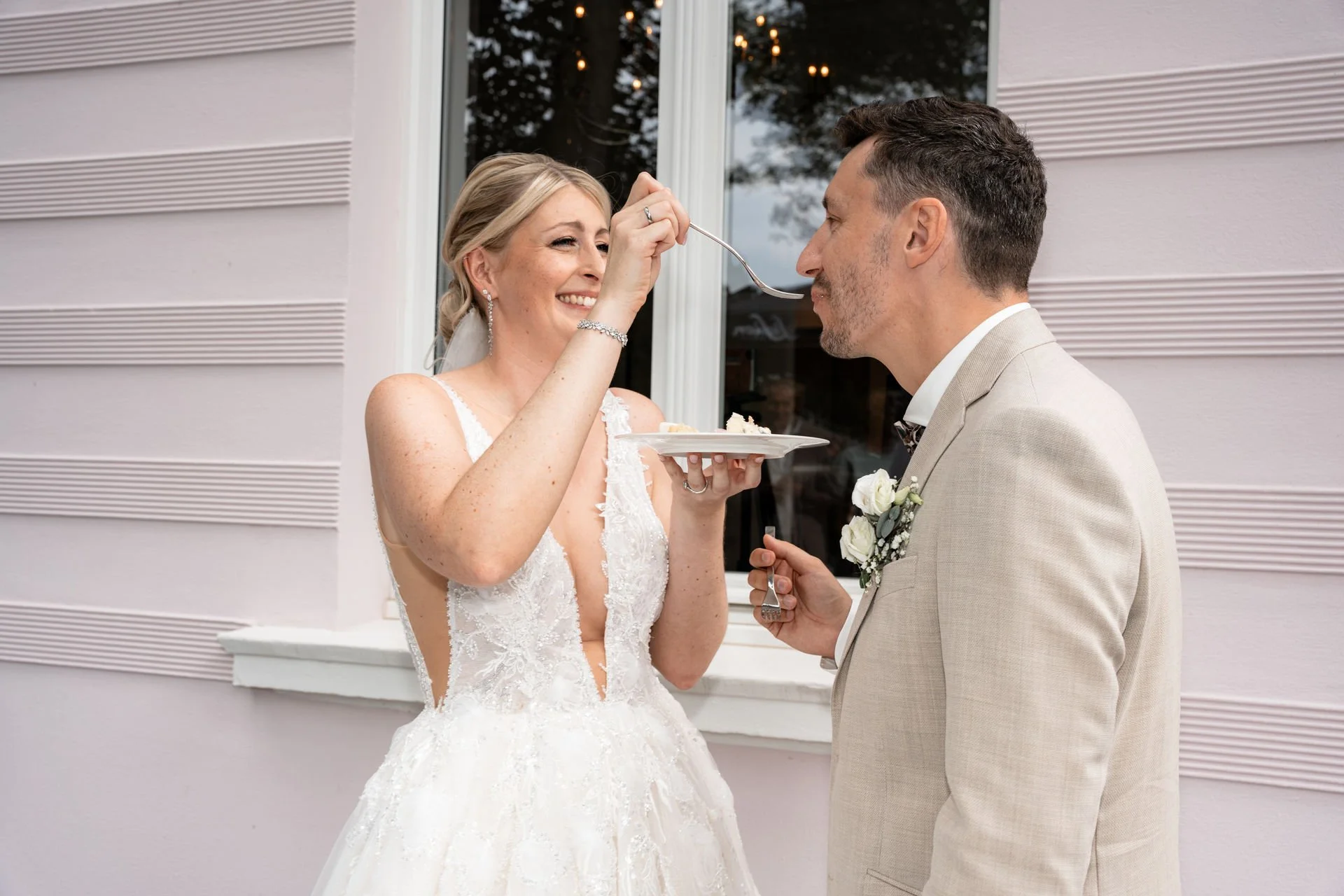 Braut füttert Bräutigam mit Hochzeitskuchen bei ihrer Hochzeit im Freien.