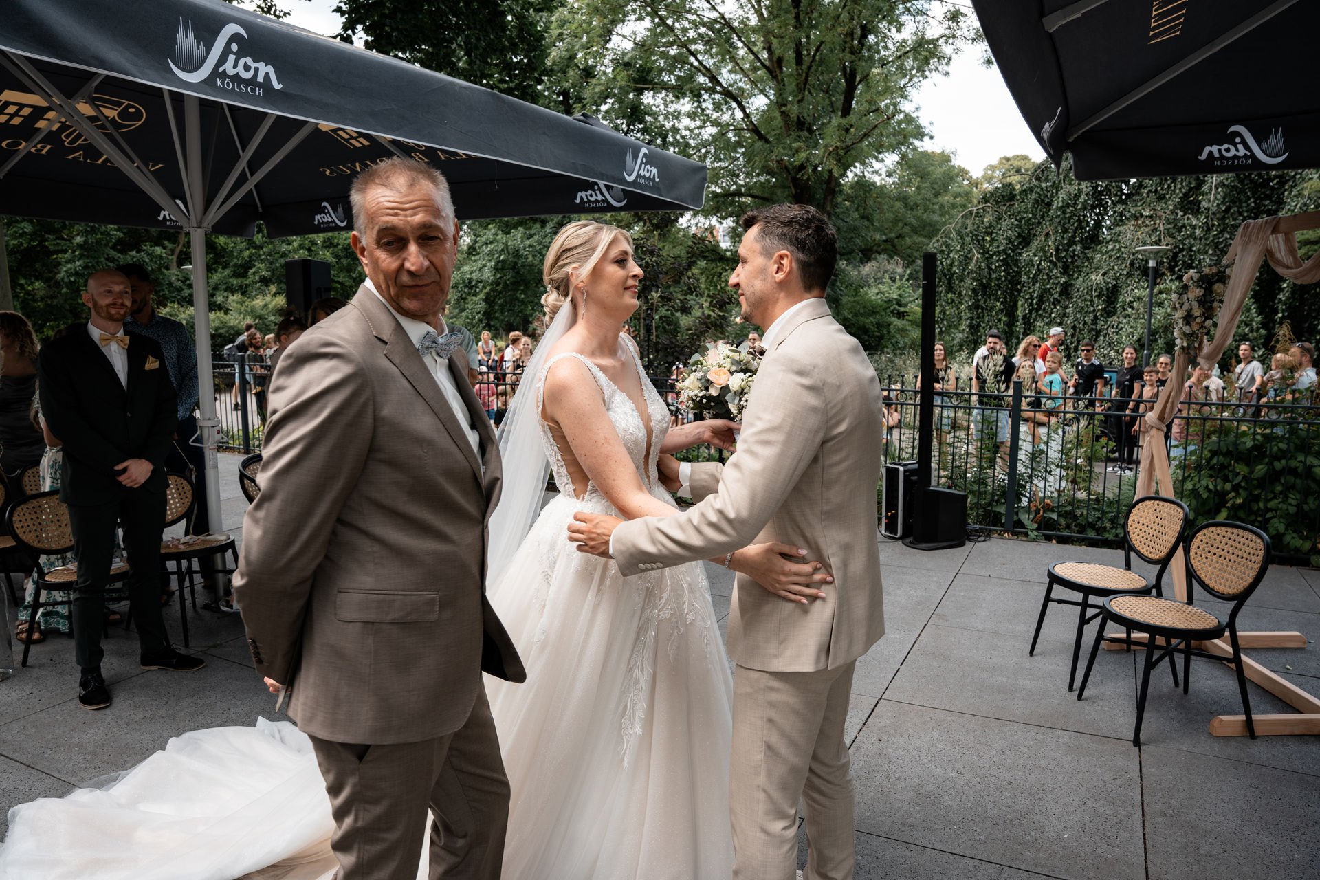 Ein Brautpaar bei einer Zeremonie, umgeben von Gästen im Freien.