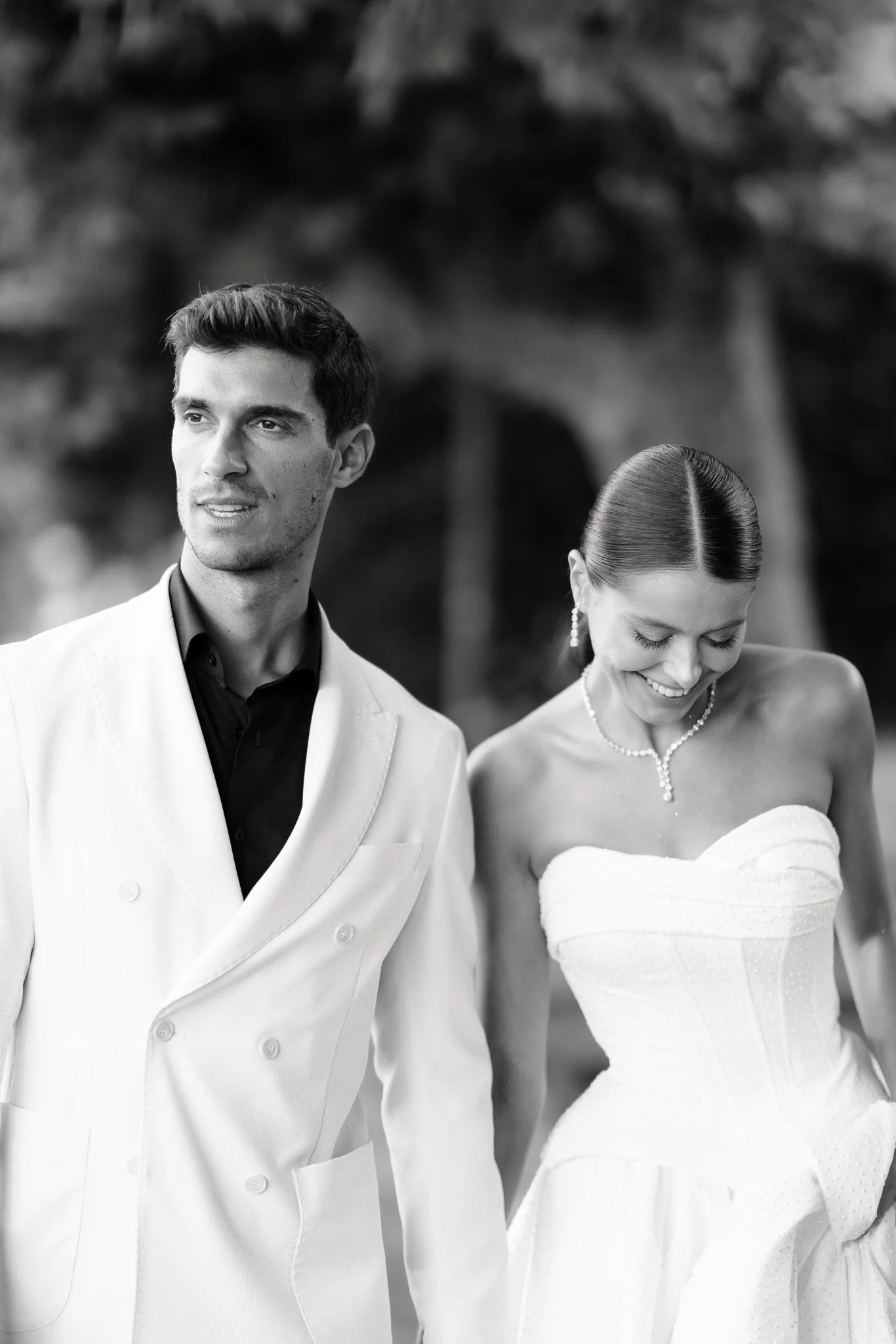 Ein Mann und eine Frau in formeller Kleidung, vermutlich bei einer Hochzeit, in einem Park, schwarz-weiß Fotografie.