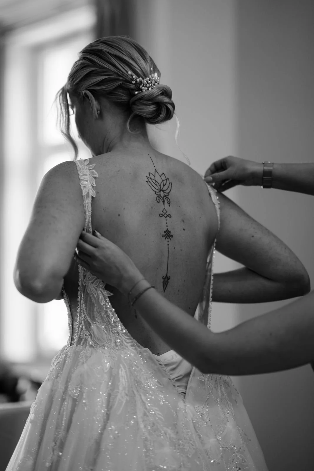 Braut wird in einem Hochzeitskleid mit Spitze und Pailletten für die Zeremonie vorbereitet, während jemand ihr ein Handgelenk befestigt.