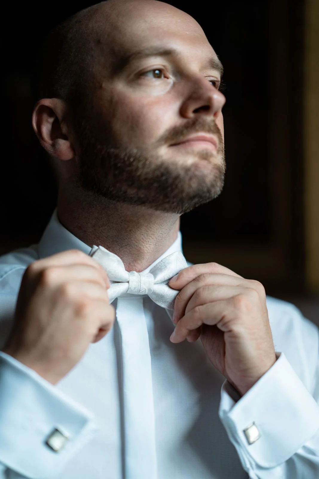 Ein Mann in formeller Kleidung richtet eine weiße Fliege zu, Nahaufnahme des Gesichts und der Hände.