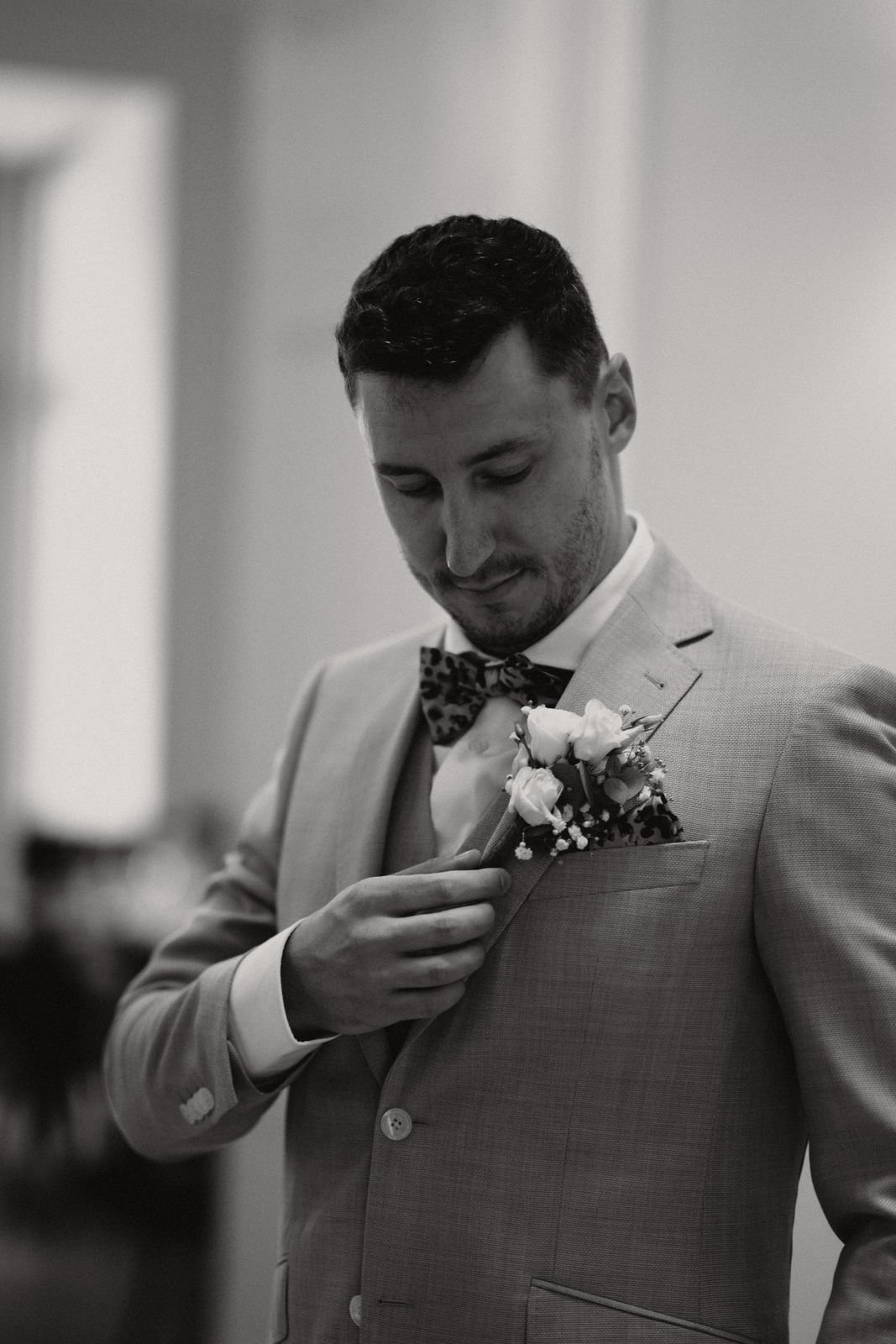 Mann in Anzug und Fliege, der eine Anstecknadel mit Blumen auf seine Jacke steckt.