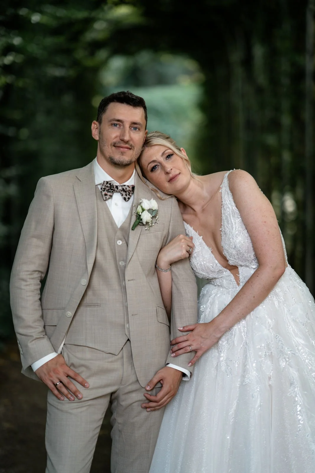 Ein verliebtes Brautpaar in einer Waldkulisse, das an seiner Hochzeit im eleganten Hochzeitskleid und Anzug steht.