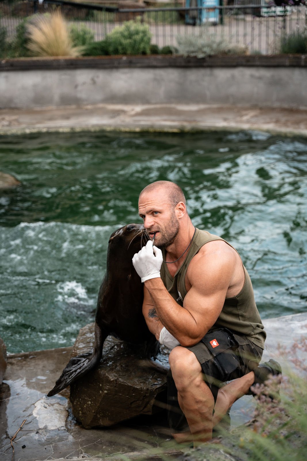 Ein Mann im Schwimmbad mit einem Seehund, der ihm eine Fingerwaffe zeigt.