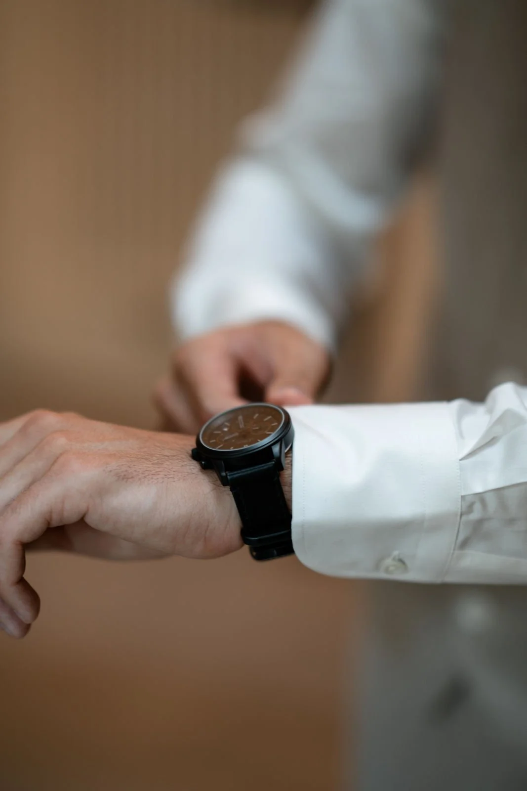 Nahaufnahme von einer Person, die eine Armbanduhr trägt, während eine andere Person die Uhrzeit überprüft, alle tragen weiße Hemden.