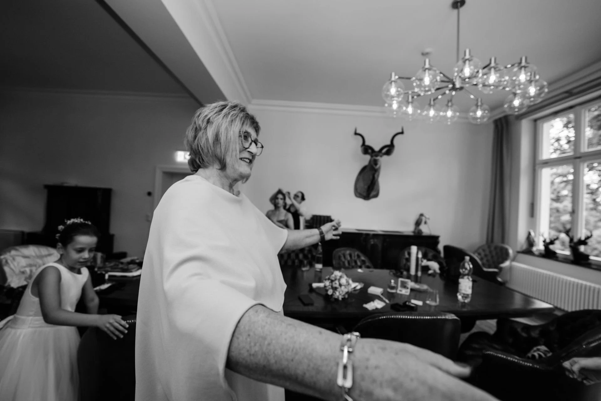 Frau und junges Mädchen in einem Wohnzimmer, dekoriert mit einem Hirschkopf und Skulpturen, vor einem Tisch voller Gegenstände.