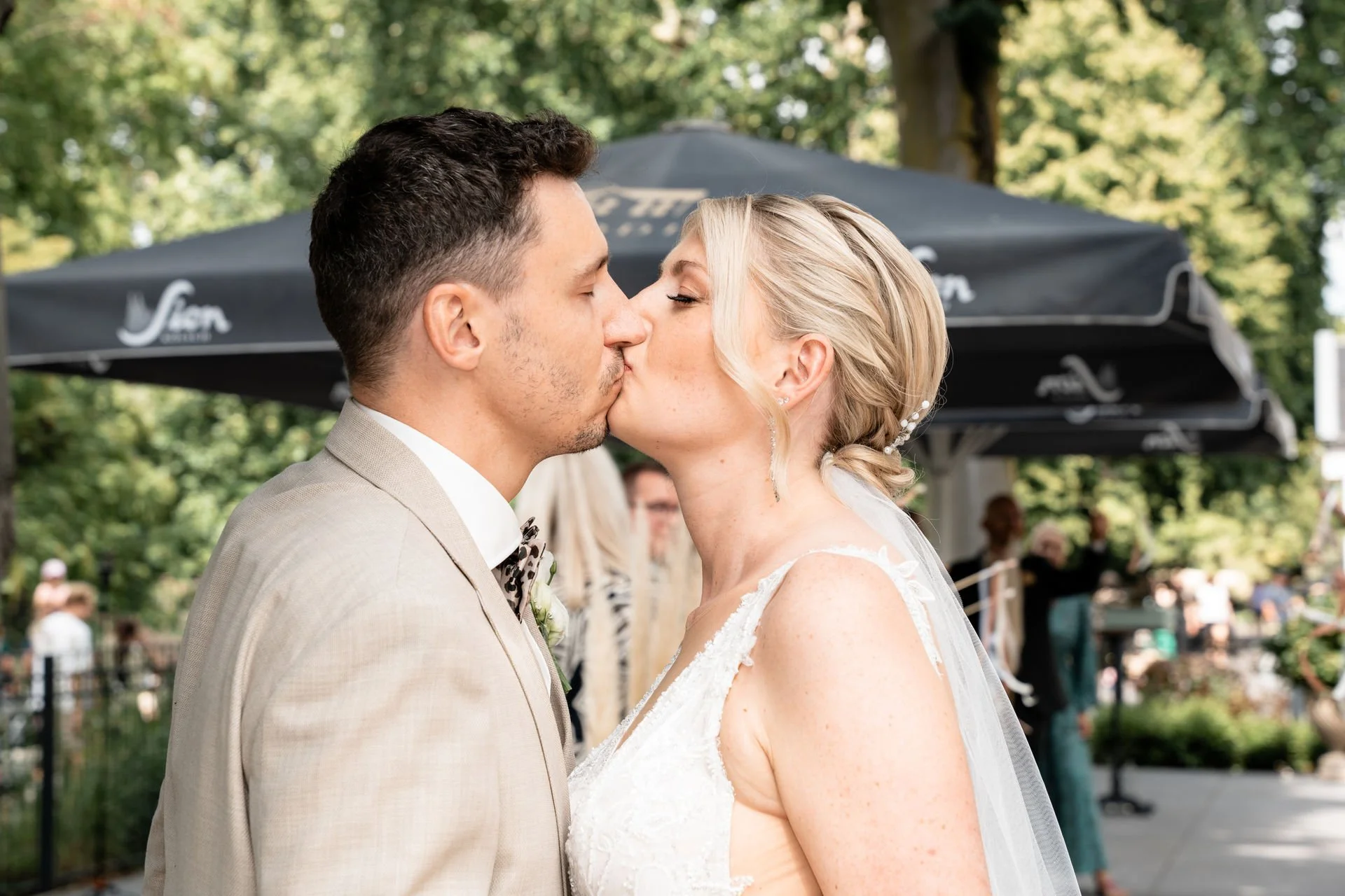 Ein frisch vermähltes Brautpaar küsst sich an einem sonnigen Tag bei einer Hochzeit im Freien.