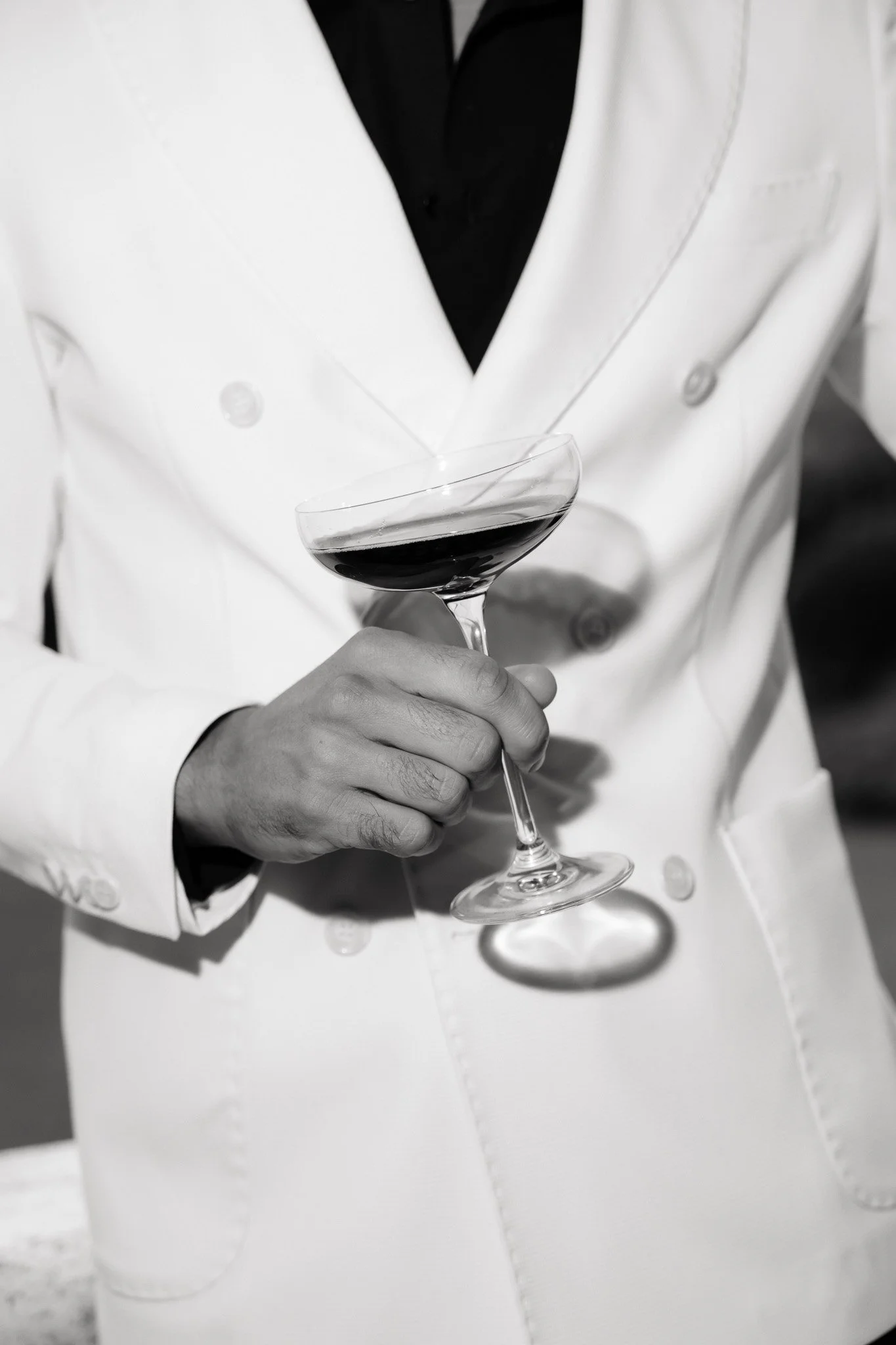 Mann in weißem Anzug hält ein Glas Rotwein