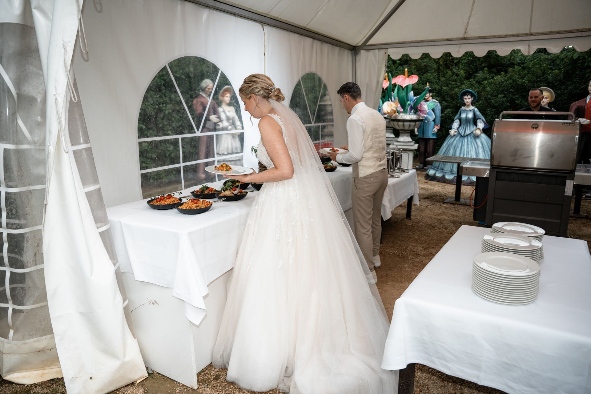 Braut in Weißes Hochzeitskleid und Bräutigam in hellen Anzügen beim Buffet.