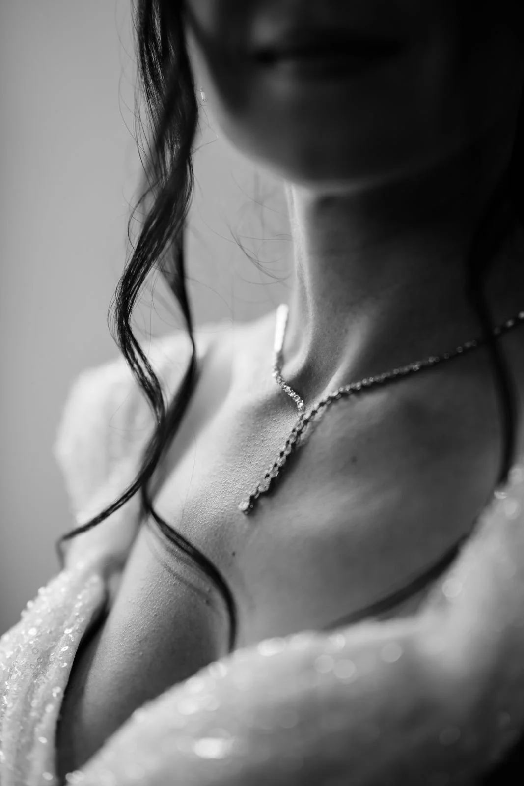 Schwarz-weiß-Foto eines schulterfreien Kleides mit einem schmalen, glänzenden Halskettchen, das die Schulter und den Hals einer Frau betont, deren Gesicht zum Teil nicht sichtbar ist.