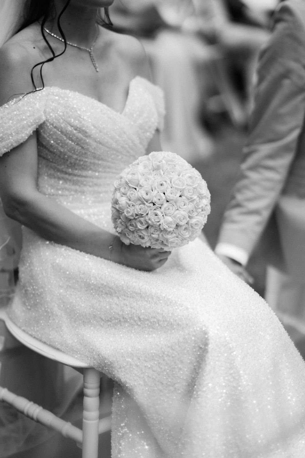 Braut in langem, glitzerndem Hochzeitskleid hält einen großen Strauß weißer Rosen bei einer Hochzeit.