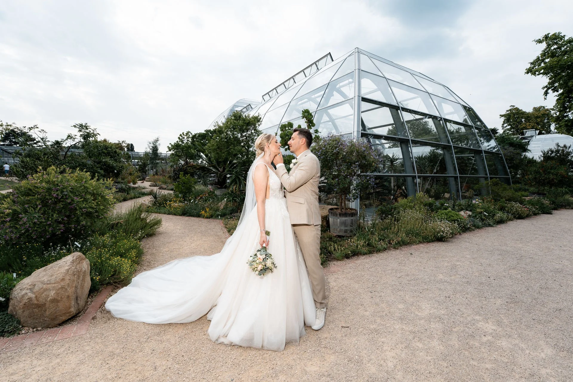 Braut und Bräutigam beim Hochzeitsshooting in einem botanischen Garten vor einem großen Glashaus.
