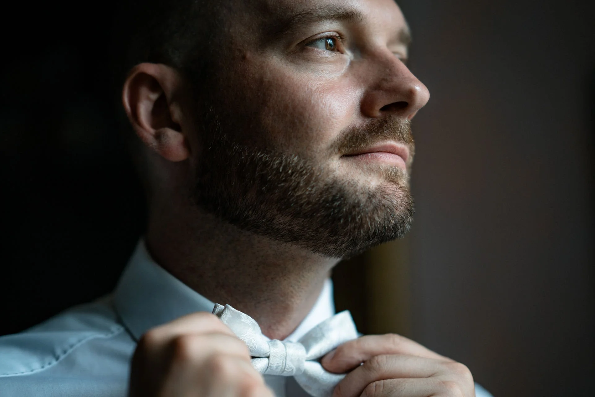 Ein Mann richtet sein weißes Hemd und bindet eine schwarze Fliege.